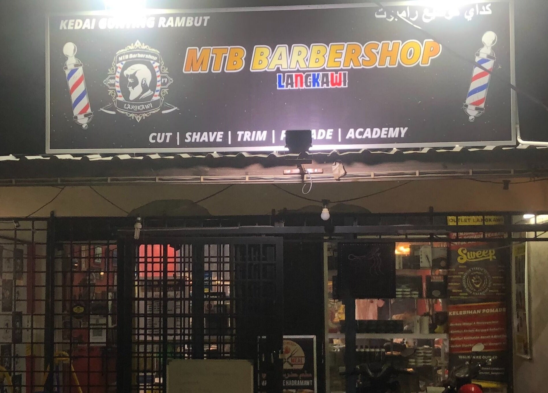 MTB Barbershop and Academy in Langkawi, Kedah, MY, lit up at night showcasing its vibrant sign and entrance.