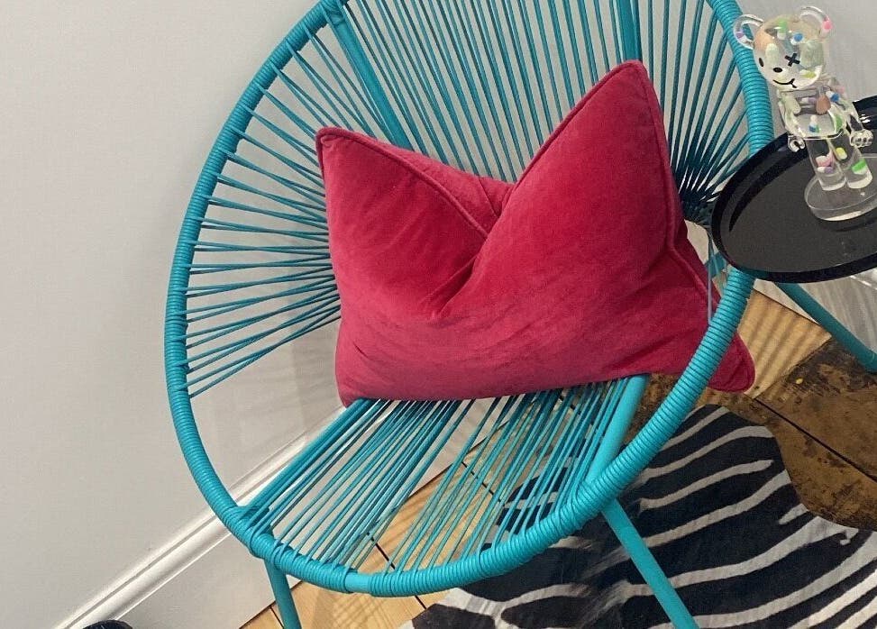 Stylish turquoise chair with pink pillow at Get Waxed, Gloucester, England, GB, offering modern comfort.