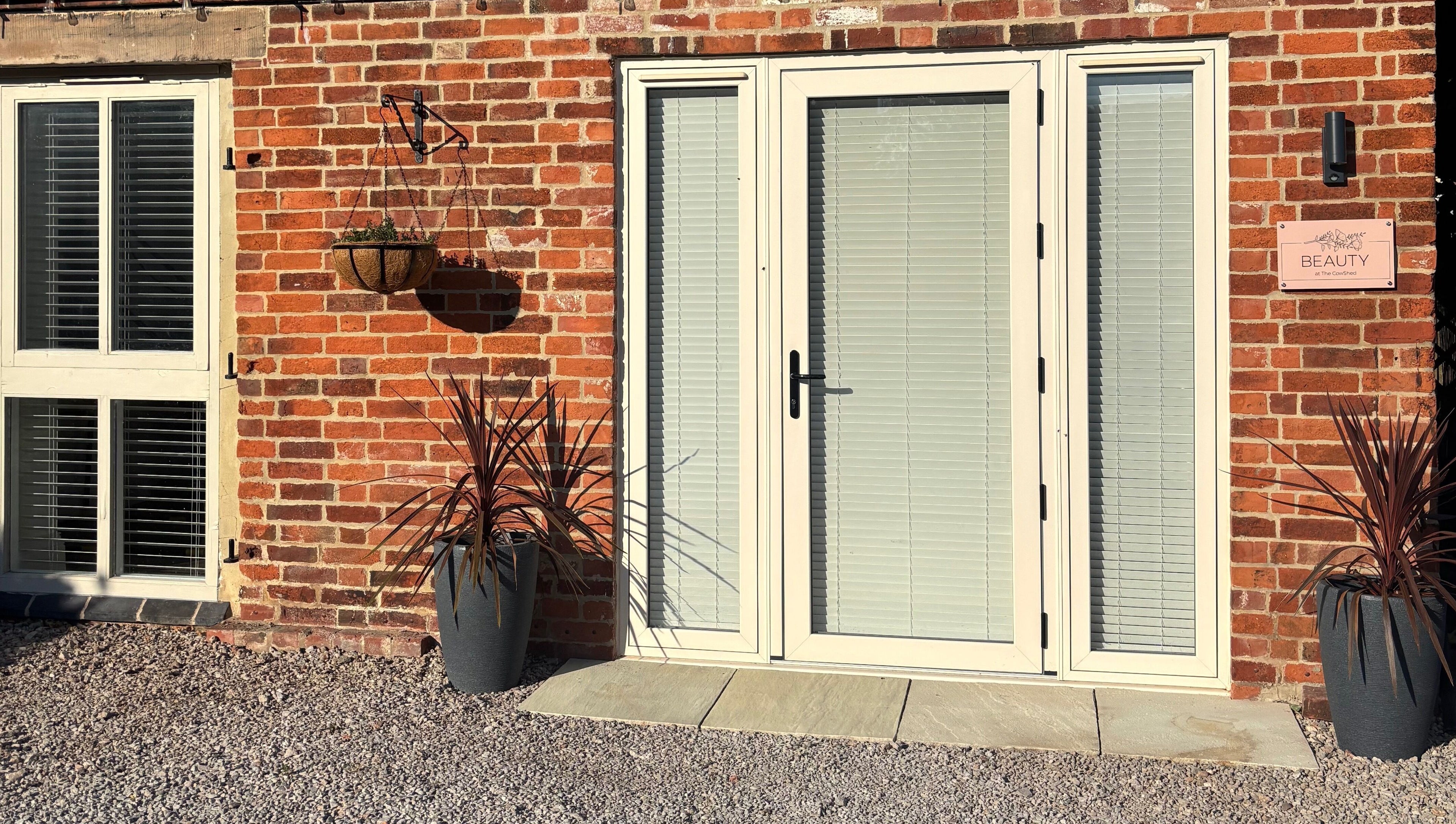 Charming brick entryway of Beauty at The CowShed in Uttoxeter, England, GB, featuring potted plants and hanging basket.
