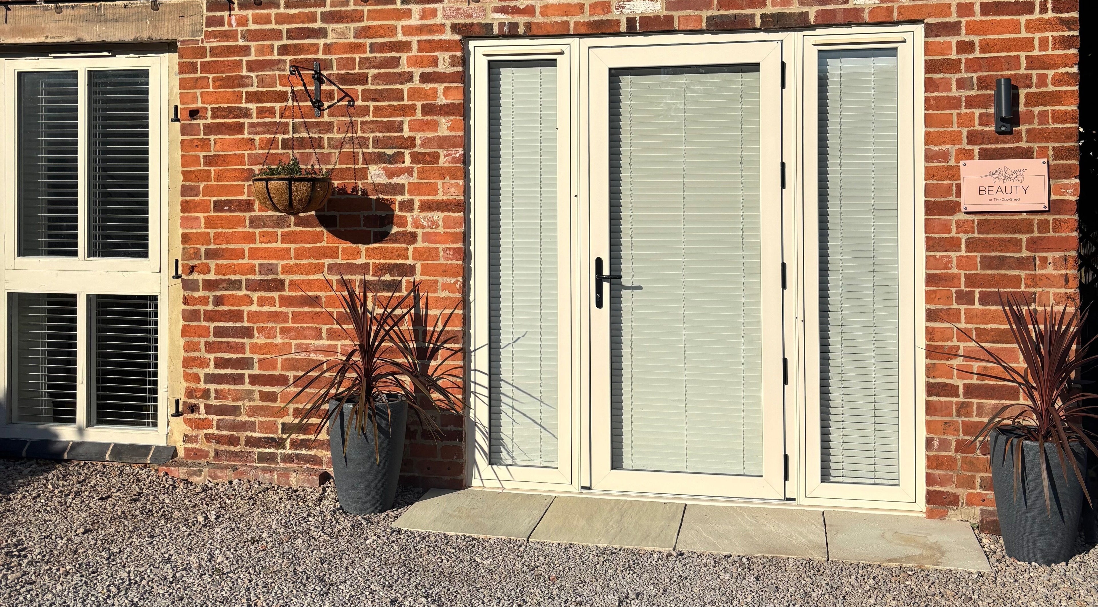 Charming brick entryway of Beauty at The CowShed in Uttoxeter, England, GB, featuring potted plants and hanging basket.