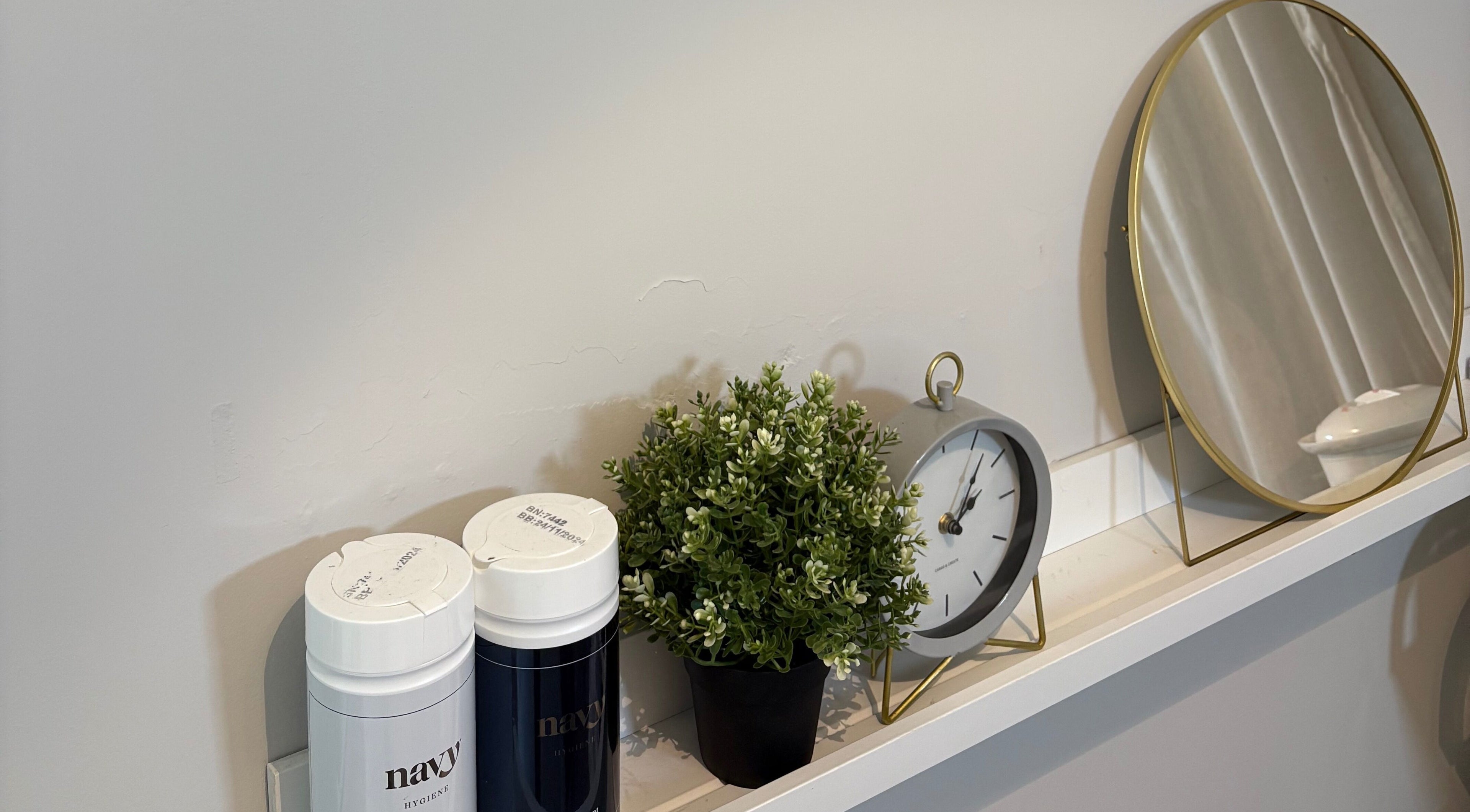 Elegant shelf with decor at Mark One Beauty, Exeter, England, GB, featuring a clock, mirror, and plant.