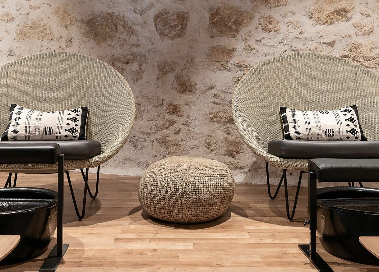 Αναπαυτικές καρέκλες στο Apotheke Spa, Χανιά, GR με διακοσμητικά μαξιλάρια και πέτρινη διακόσμηση.