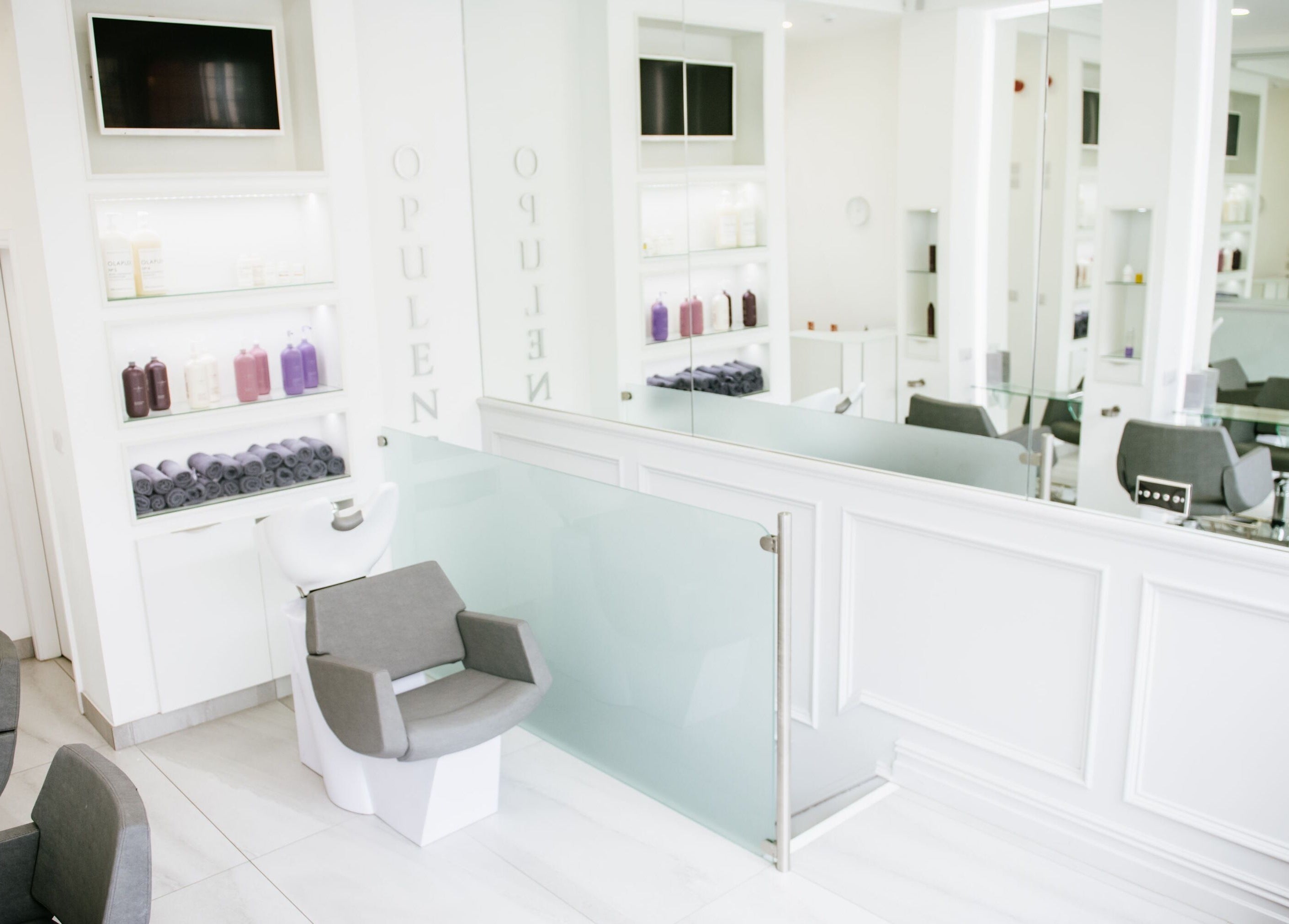 Bright interior of Opulence Hairdressing in Lytham Saint Annes, England, GB, featuring sleek chairs and mirrored walls.