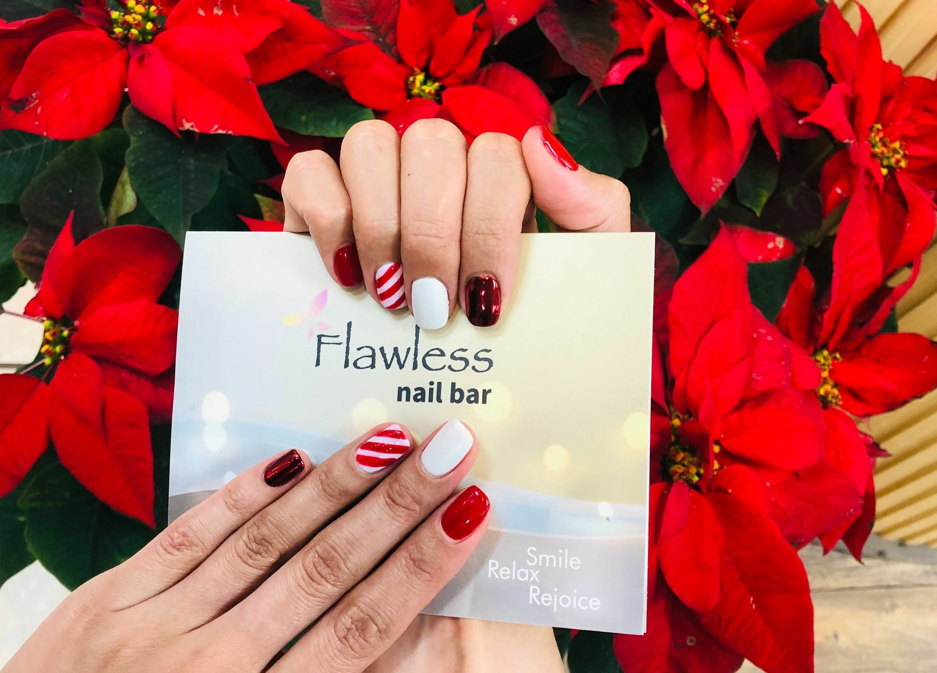 Holiday-themed manicured hands at Flawless Nail Bar, Denver, Colorado, US with poinsettia backdrop.