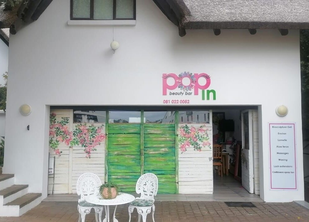 Entrance of Pop in Beauty Bar in Saint Francis Bay, ZA with floral doors and patio seating.