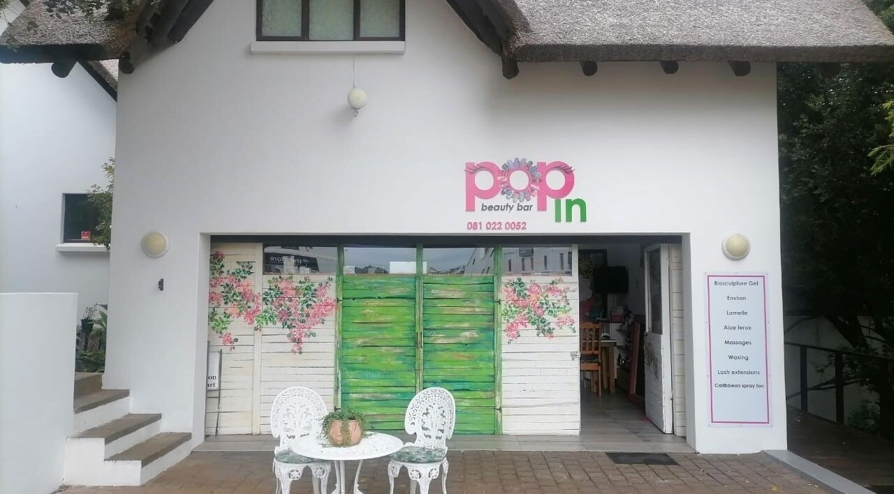 Entrance of Pop in Beauty Bar in Saint Francis Bay, ZA with floral doors and patio seating.