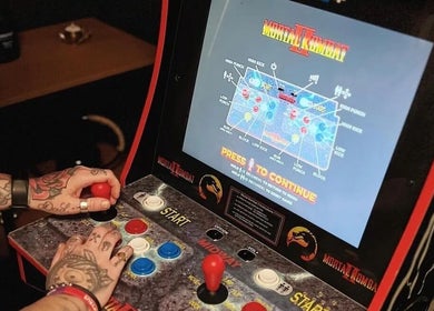 Tattooed hands playing Mortal Kombat II at New Street Collective, Bridge Of Allan, Scotland, GB.