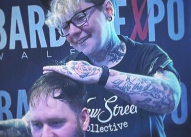 Tattooed barber styling hair at New Street Collective, Bridge Of Allan, Scotland, GB.