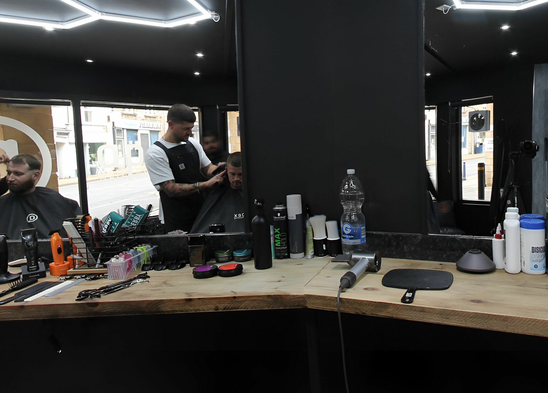 Stylists grooming clients at Apex Male Grooming, Morpeth, England, GB. Tools set on wooden counter.