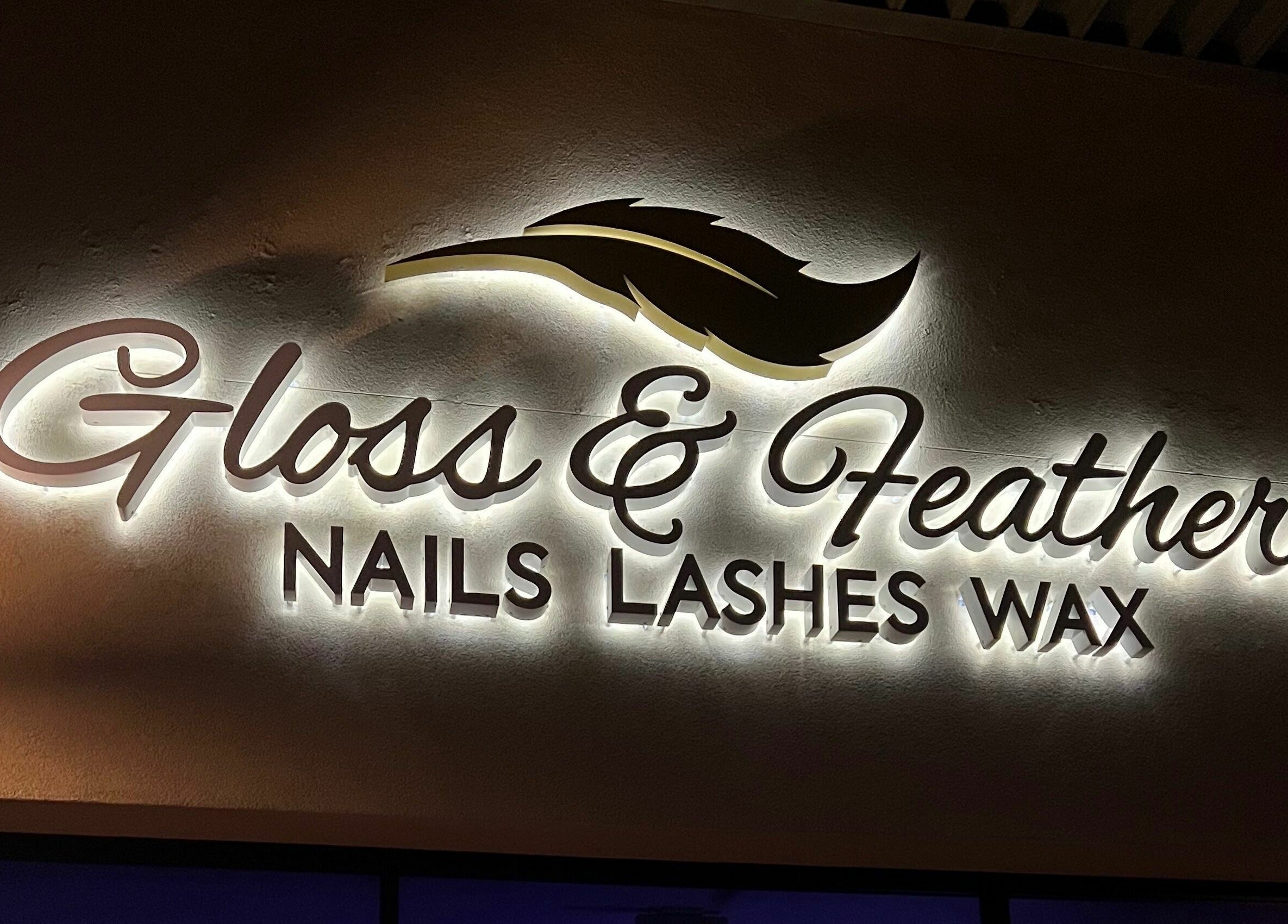 Illuminated sign of Gloss and Feathers (Nails. Lashes. Wax.) in Phoenix, Arizona, US against a night backdrop.