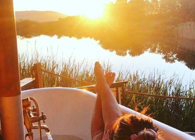 Outdoor bathtub at sunset at Go Brown Plettenberg Bay, Eastern Cape, ZA beside a tranquil river view.