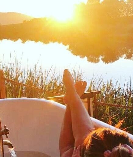Outdoor bathtub at sunset at Go Brown Plettenberg Bay, Eastern Cape, ZA beside a tranquil river view.