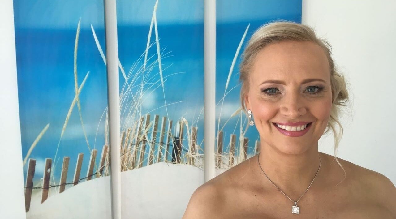 Smiling woman in Go Brown Durbanville Studio, Durbanville, Western Cape, ZA with beach art backdrop.