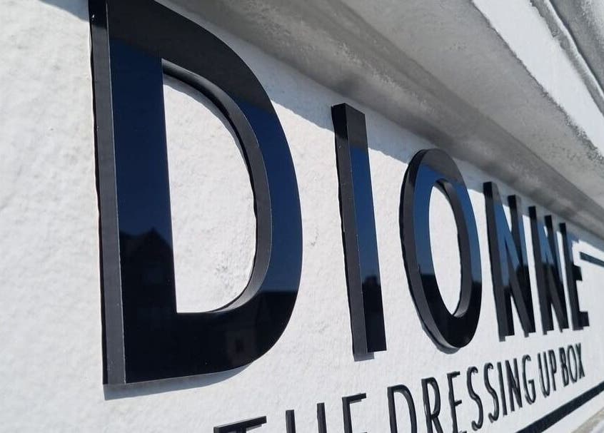 Sign of Dionne The Dressing Up Box Permanent Makeup & Training Academy in Bolton, England, GB captured under blue sky.