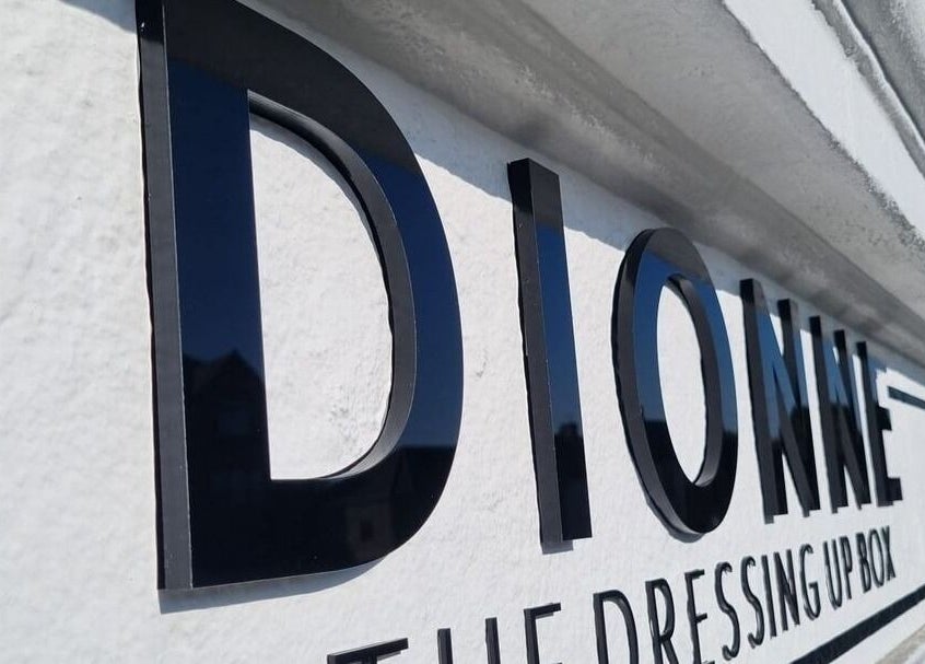 Sign of Dionne The Dressing Up Box Permanent Makeup & Training Academy in Bolton, England, GB captured under blue sky.