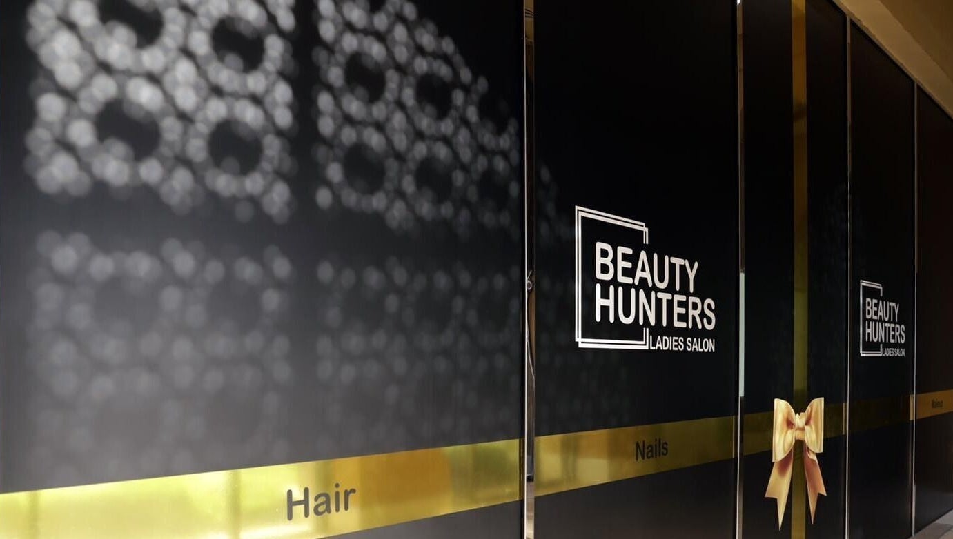 Entrance of Beauty Hunters The Pearl in Doha, QA with elegant signage and decorative gold bow.