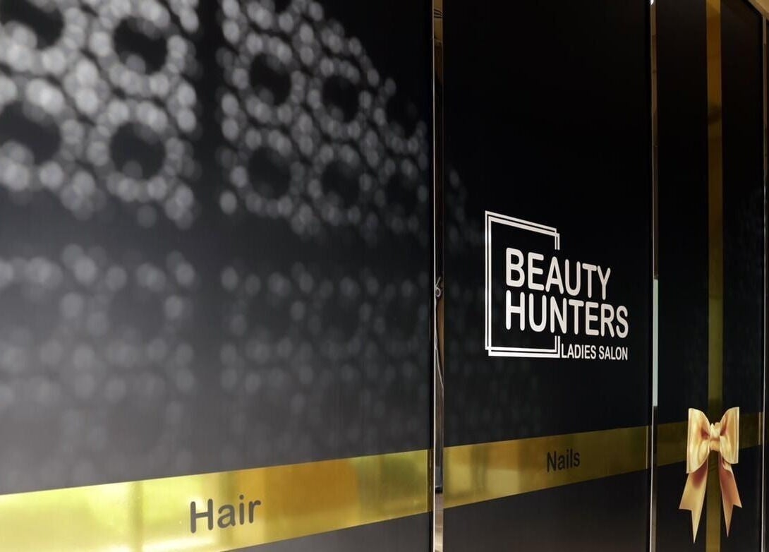 Entrance of Beauty Hunters The Pearl in Doha, QA with elegant signage and decorative gold bow.