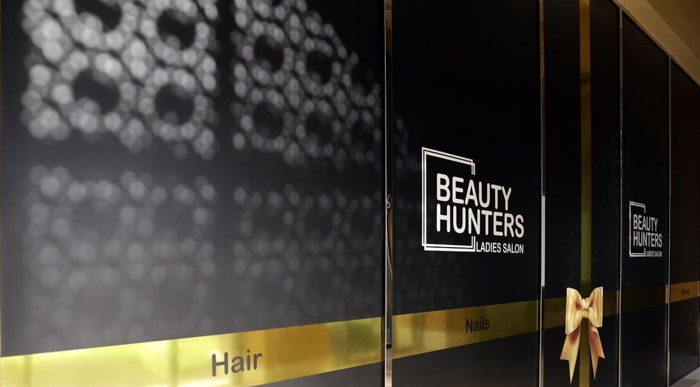 Entrance of Beauty Hunters The Pearl in Doha, QA with elegant signage and decorative gold bow.