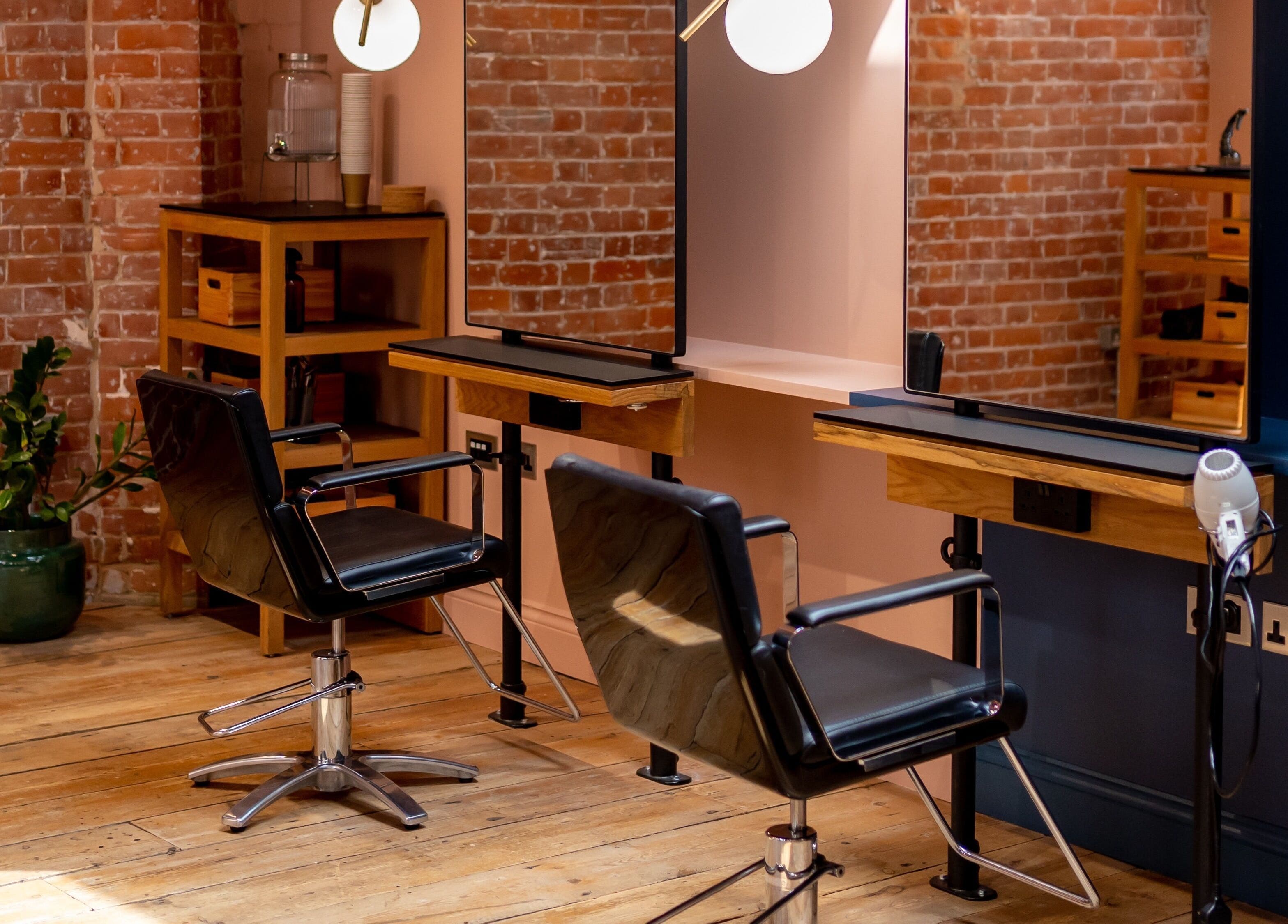 Stylish salon interior at Bond in London, England, GB with modern chairs and mirrors against brick walls.