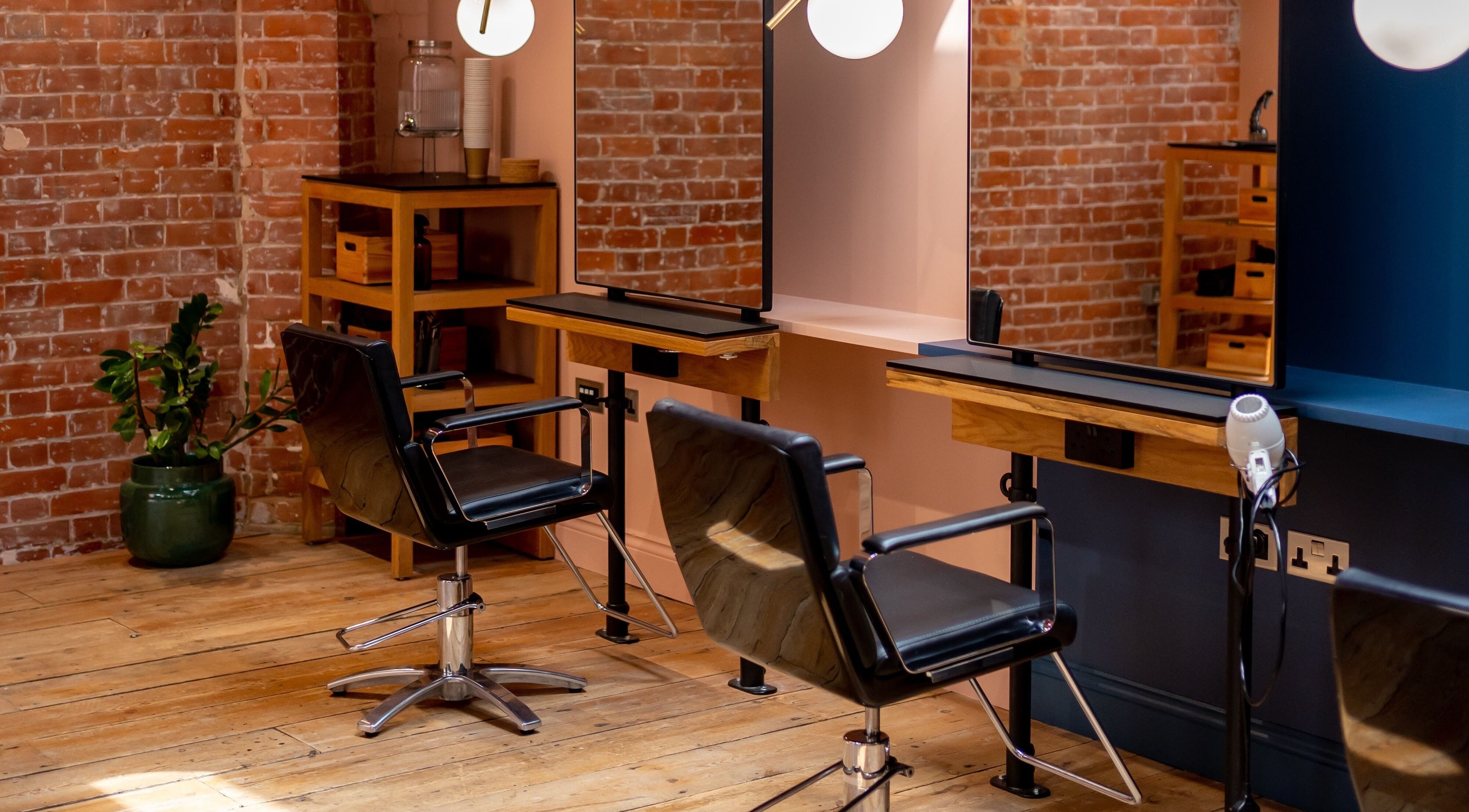 Stylish salon interior at Bond in London, England, GB with modern chairs and mirrors against brick walls.