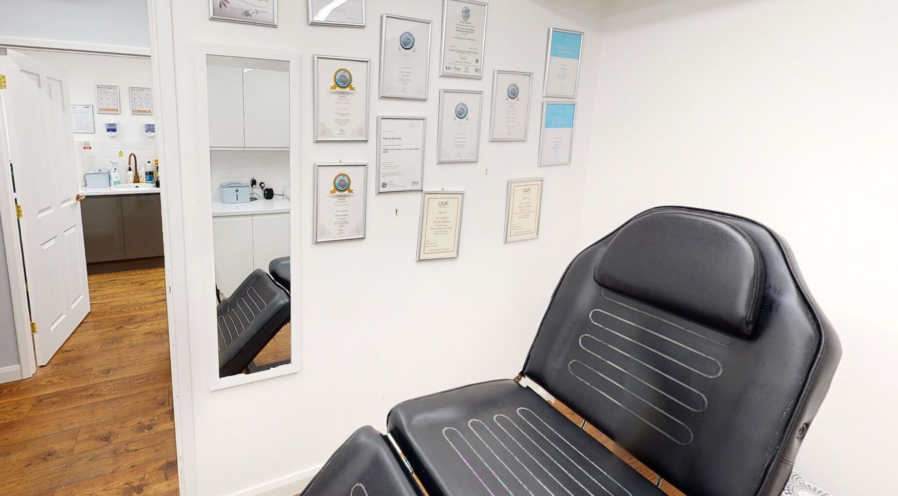 Professional certificates adorn the wall at The Avalon Rooms, Witney, England, GB, beside a sleek treatment chair.