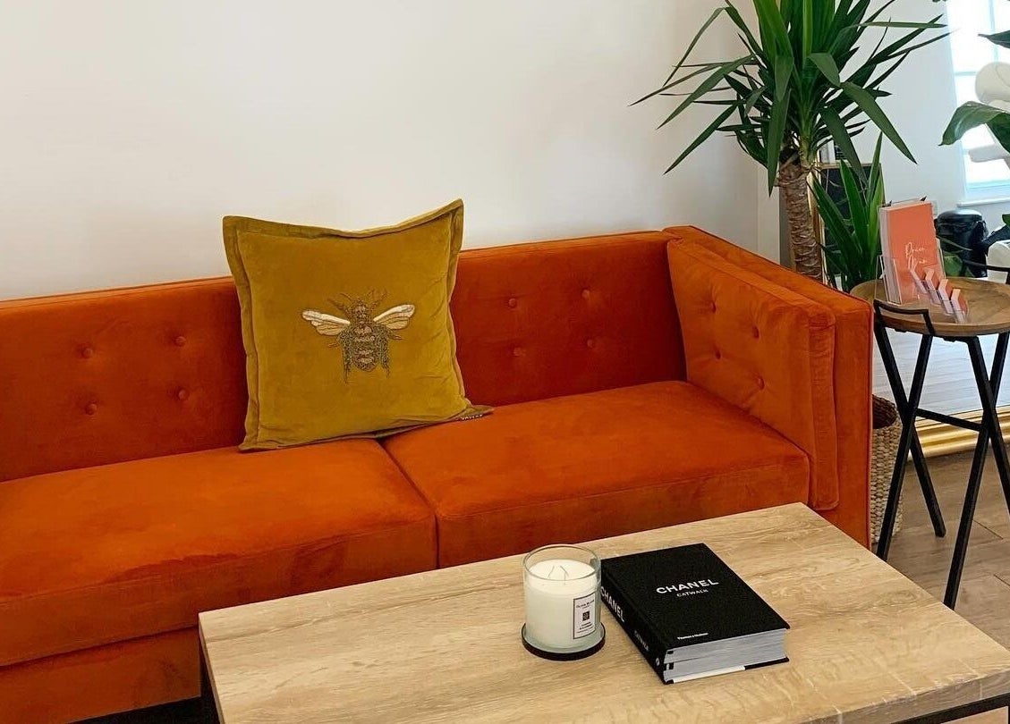 Cozy orange sofa at Flawless By Ffion in Abergavenny, Wales, GB, adorned with bee pillow and green plants.