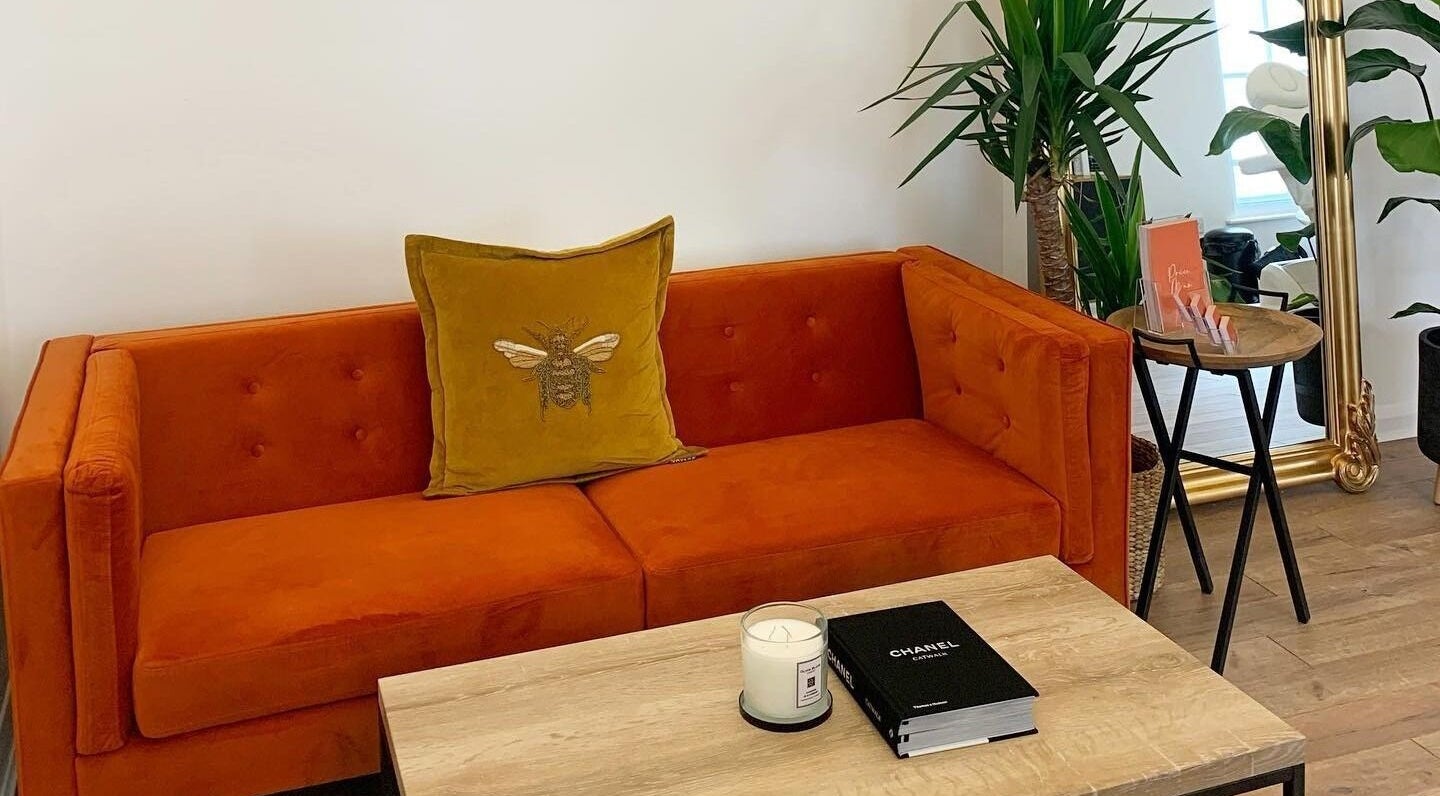 Cozy orange sofa at Flawless By Ffion in Abergavenny, Wales, GB, adorned with bee pillow and green plants.