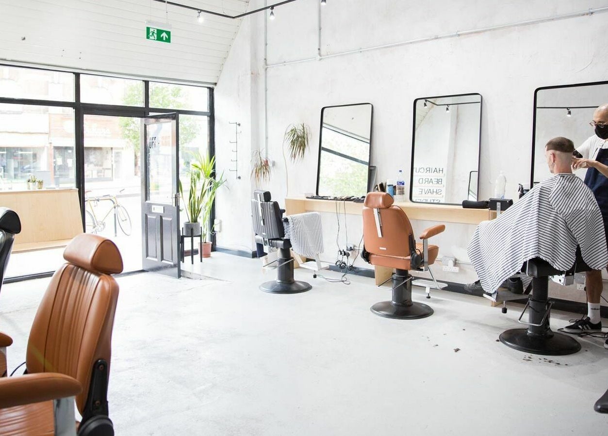 Modern barber chairs in Off Cut Streatham, London, England, GB, with stylist at work.