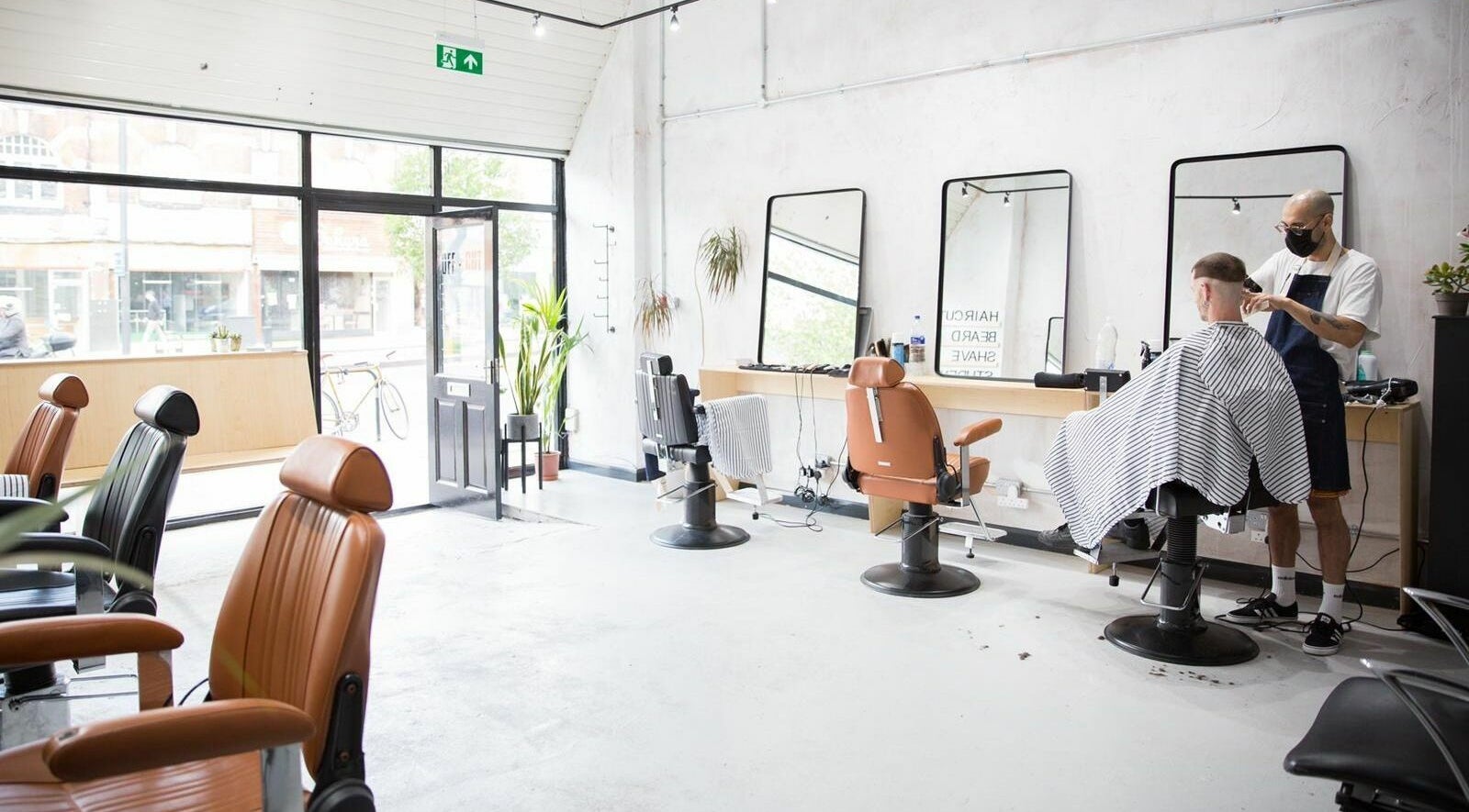 Modern barber chairs in Off Cut Streatham, London, England, GB, with stylist at work.
