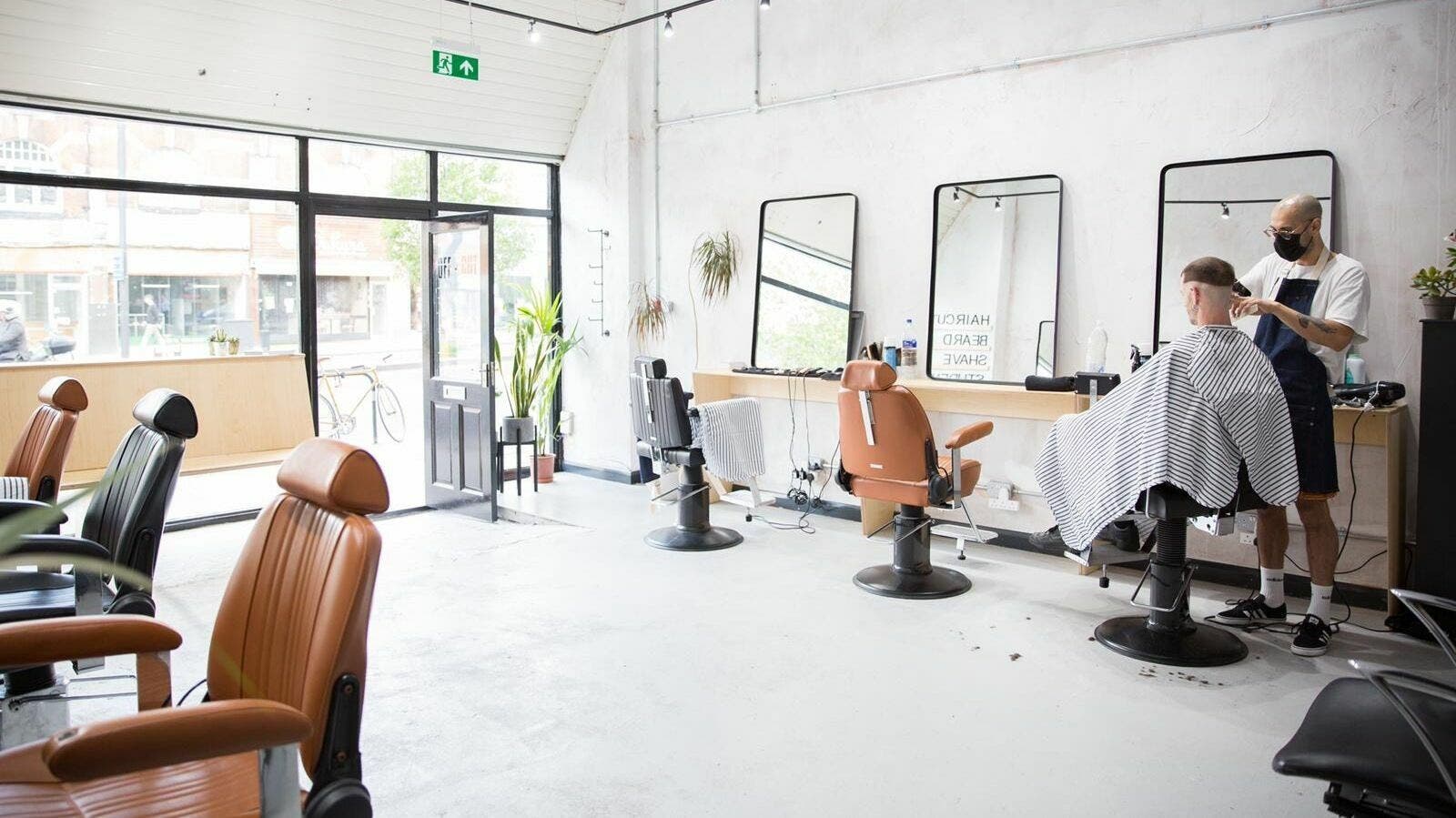 Modern barber chairs in Off Cut Streatham, London, England, GB, with stylist at work.