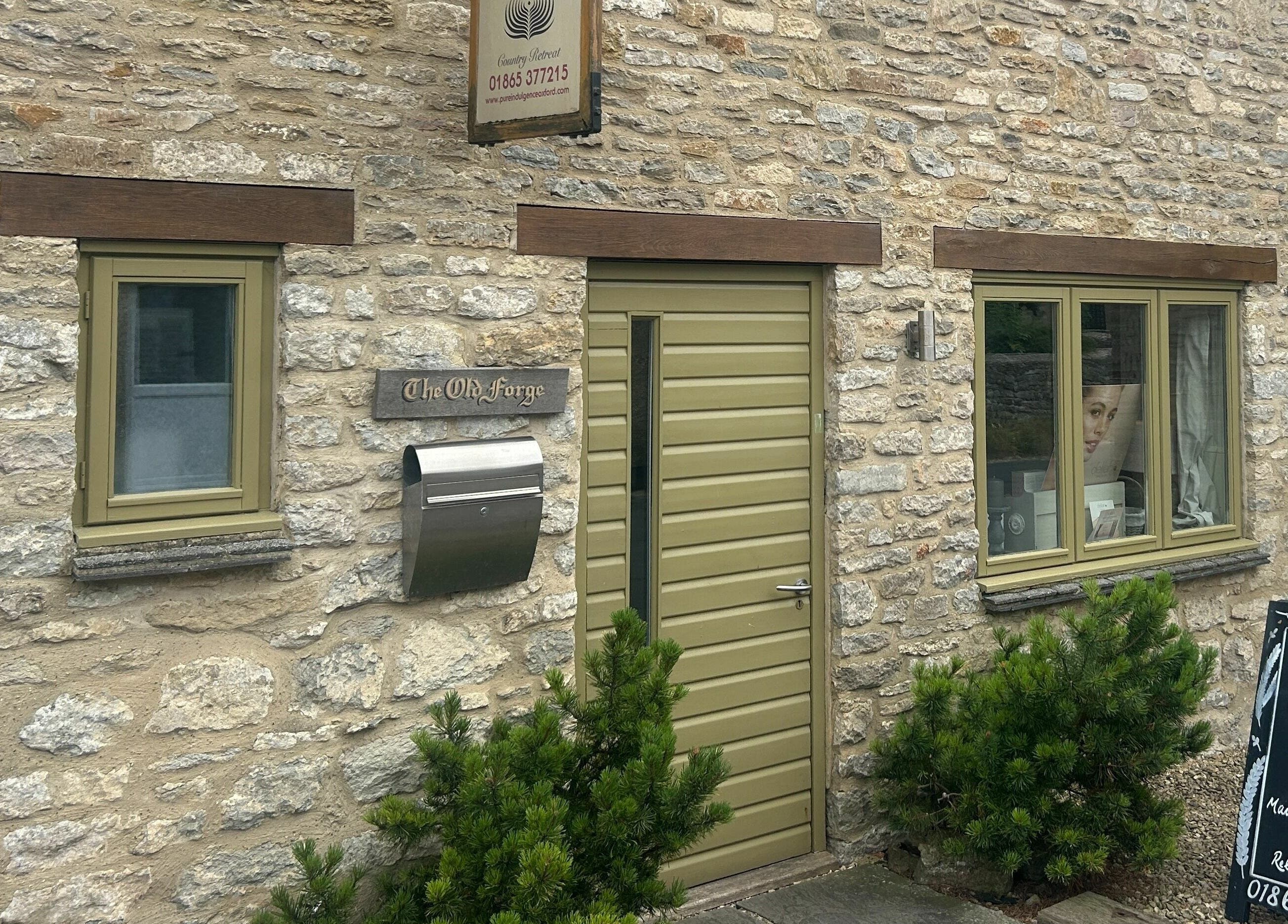 Entrance of Pure Indulgence Day Spa in Merton, England, featuring stone walls and green door.