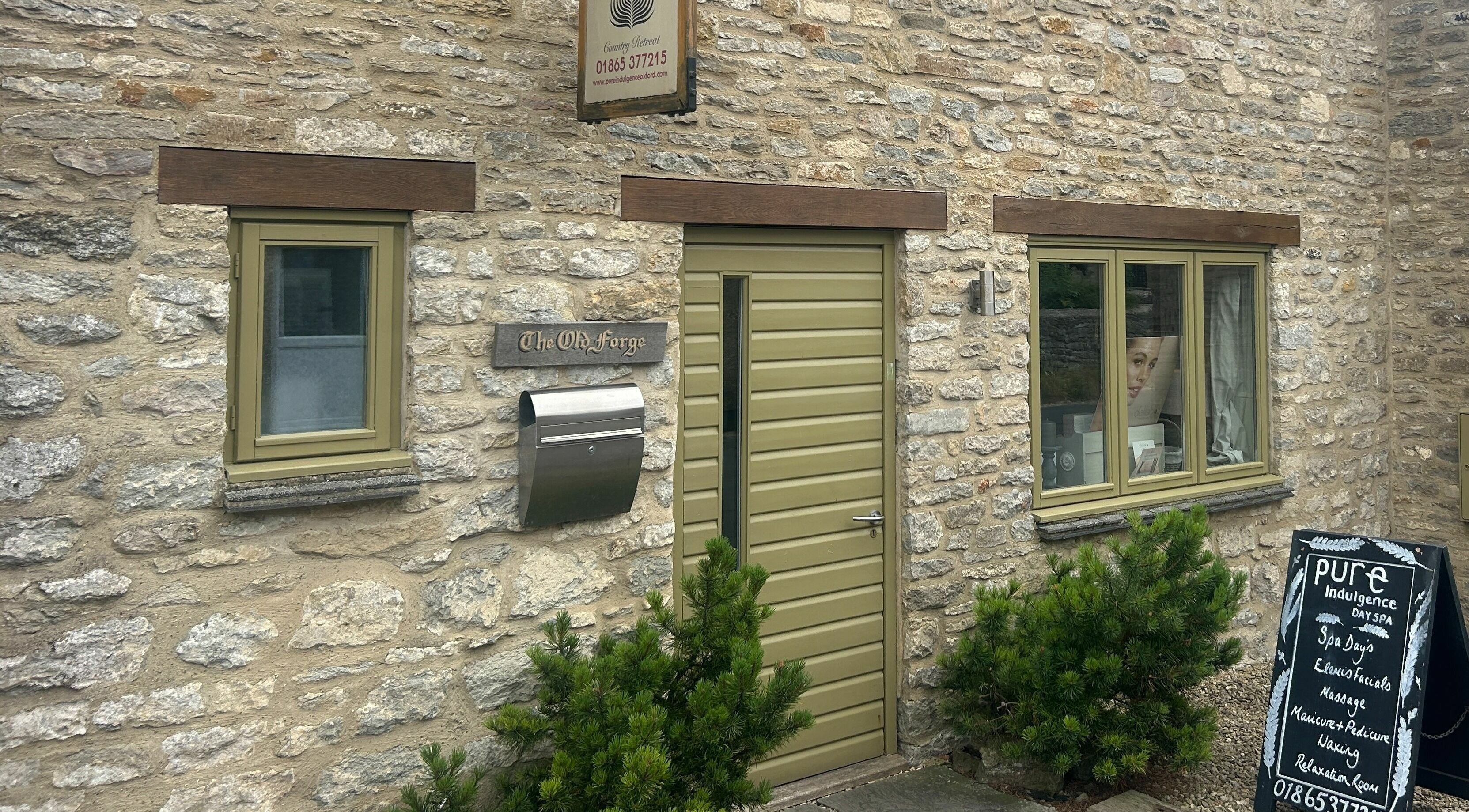 Entrance of Pure Indulgence Day Spa in Merton, England, featuring stone walls and green door.