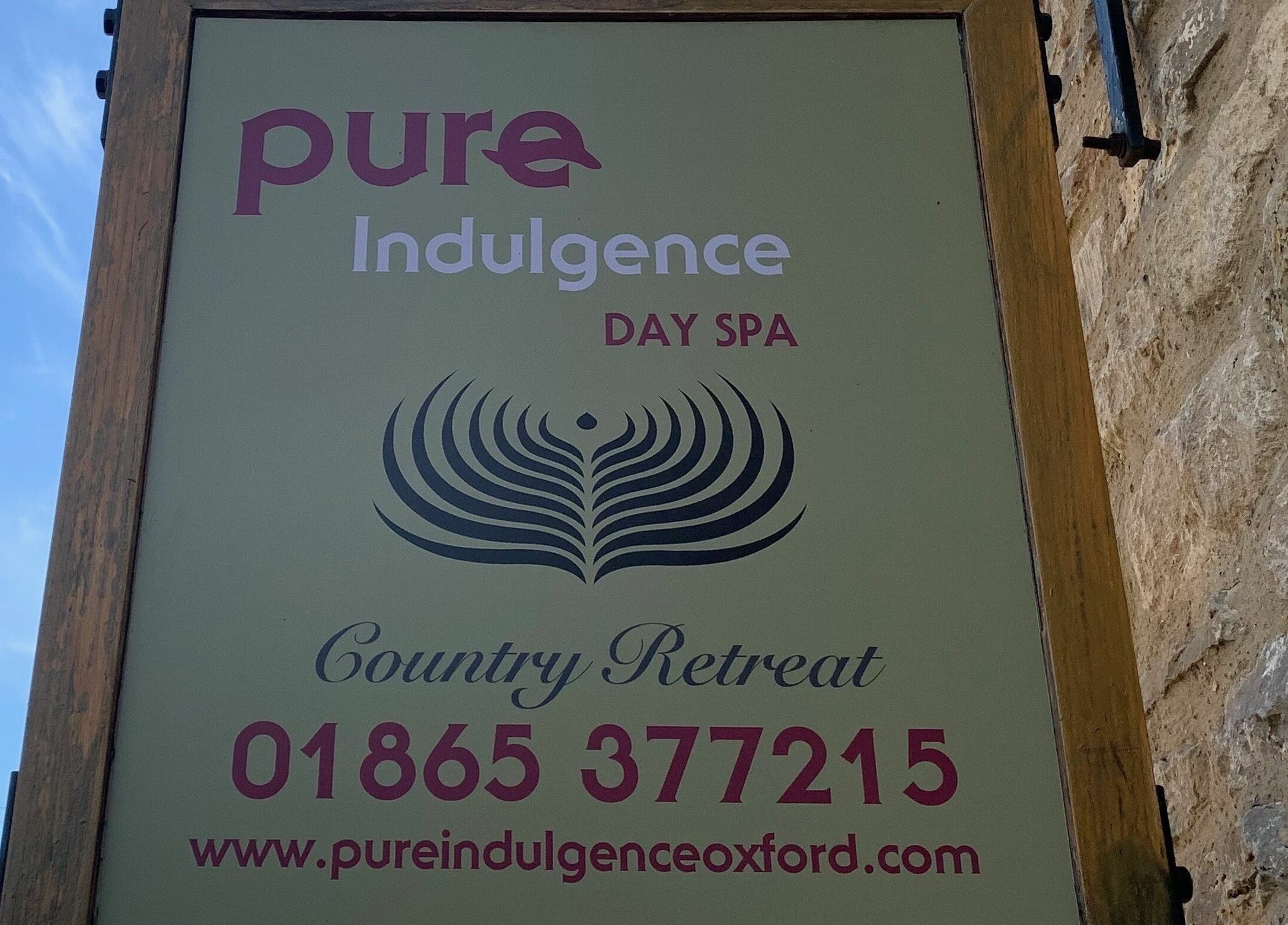 Entrance sign of Pure Indulgence Day Spa in Merton, England, GB, depicting its elegant logo under a clear sky.