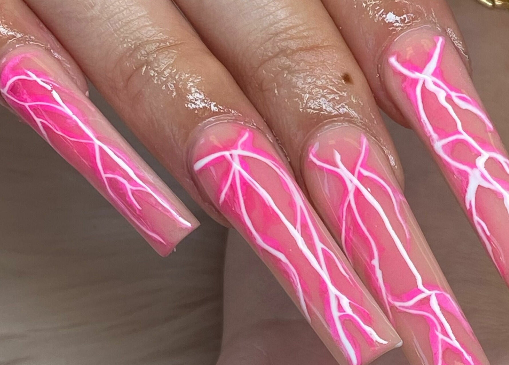 Vibrant pink nail art at Blossom Nails in Sanford, Florida, US showcasing intricate white designs.
