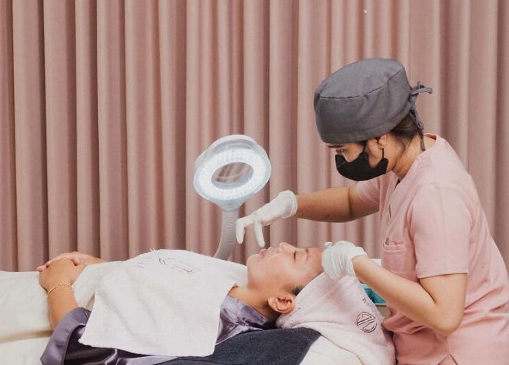 Aesthetician performing a facial treatment at Noona Glam, Bali, Bali, ID with a ring light lamp.