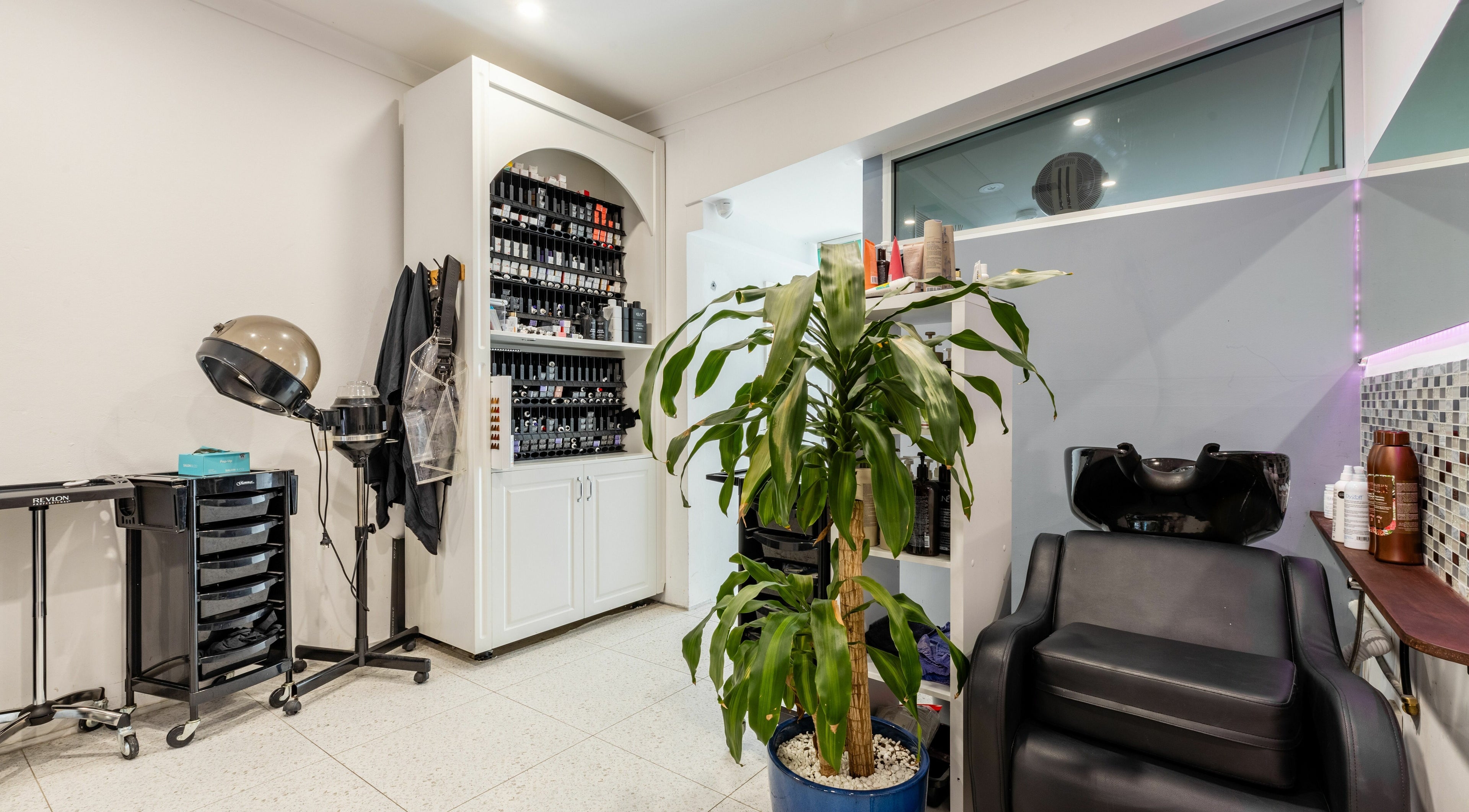 Relaxed salon corner at Collective Hair, Mascot, Pensioners 25% Off, AU. Features styling tools and plant.