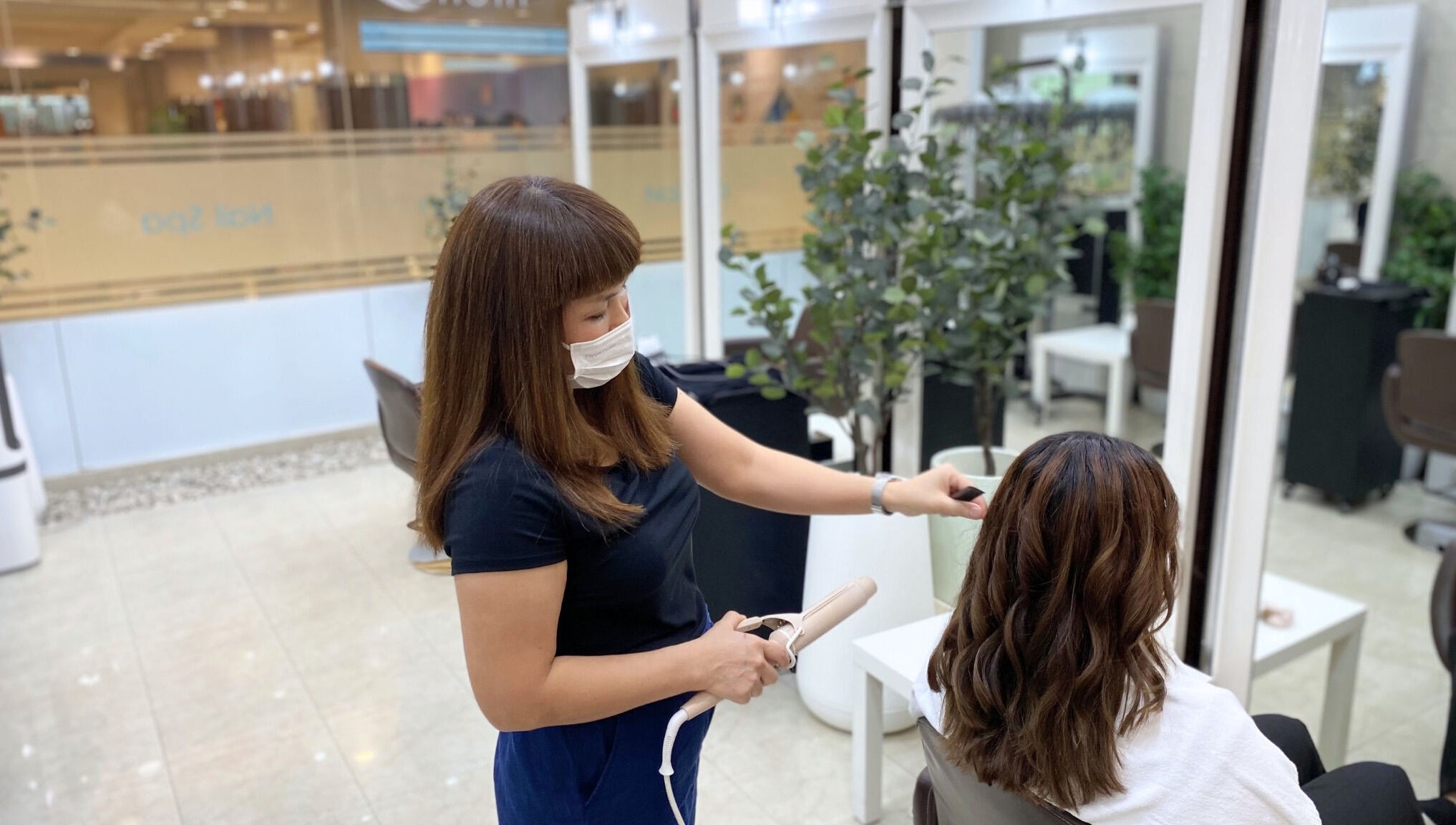 Stylist curling hair at Niche Salon Bangkok, Krung Thep Maha Nakhon, TH, creating beautiful waves.