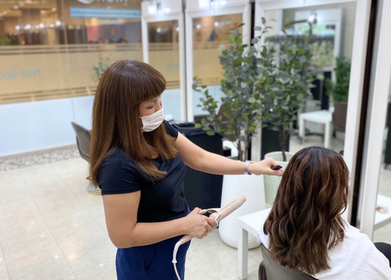 Stylist curling hair at Niche Salon Bangkok, Krung Thep Maha Nakhon, TH, creating beautiful waves.