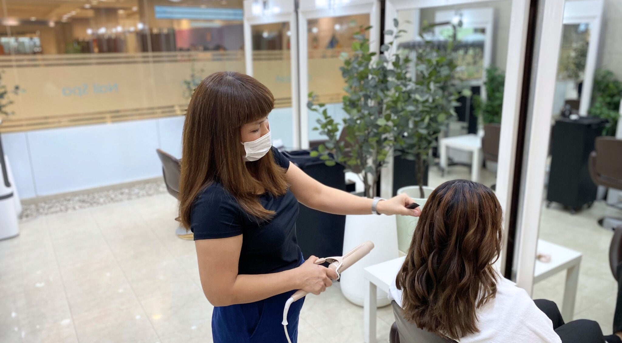 Stylist curling hair at Niche Salon Bangkok, Krung Thep Maha Nakhon, TH, creating beautiful waves.