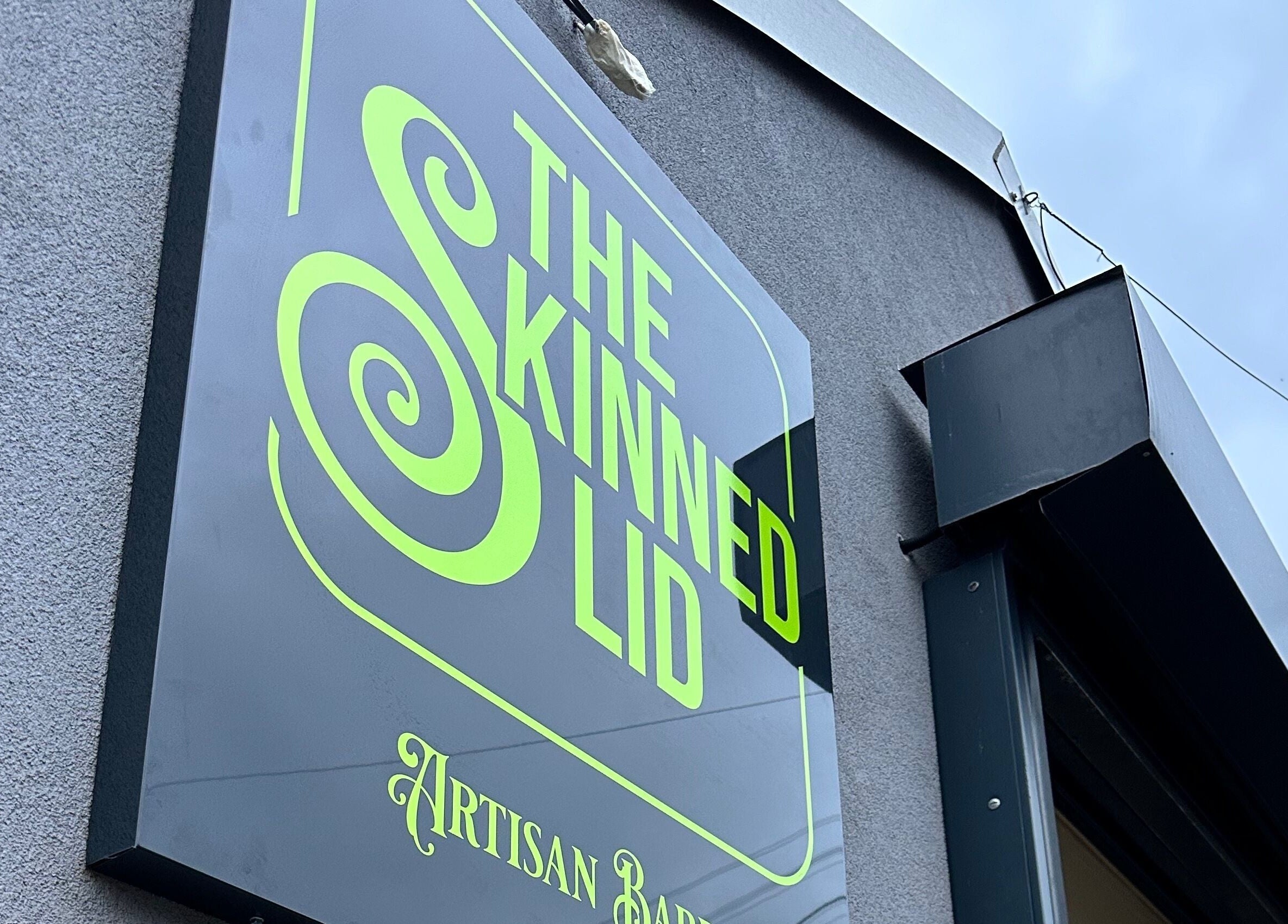 The Skinned Lid signage in Huddersfield, England, GB with vibrant design against a gray wall.