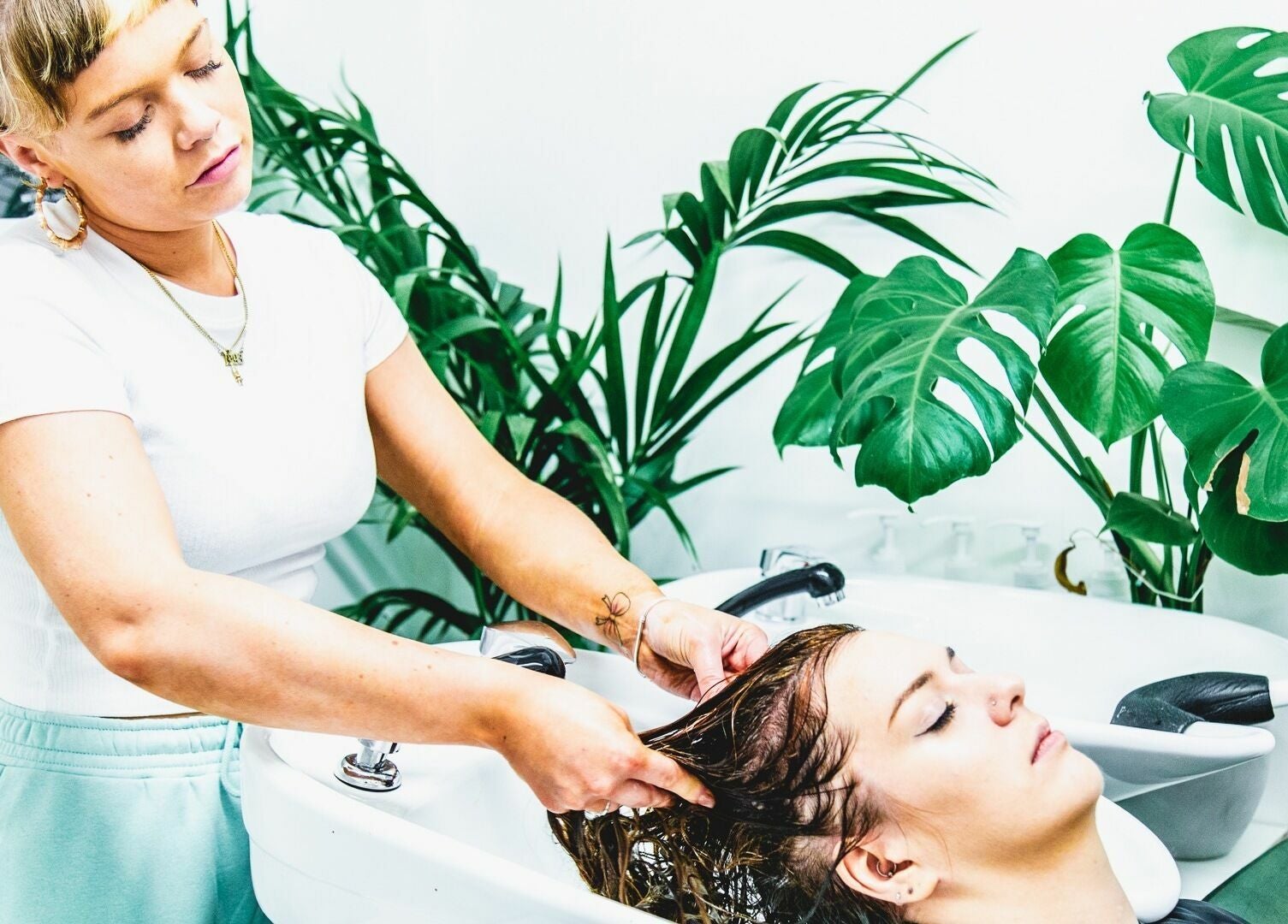 Hair stylist washing client's hair at Cuts and Creps, Bristol, England, GB amidst lush greenery.