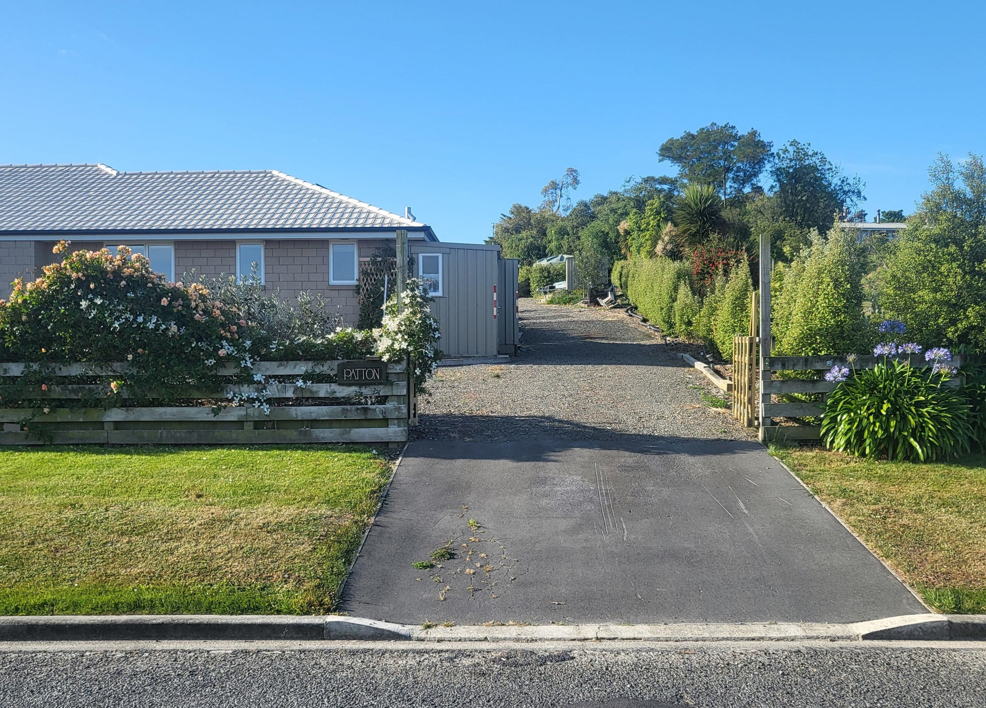 Entrance of Dr Derek Patton, Amberley, North Canterbury, NZ, featuring lush greenery and vibrant flowers.