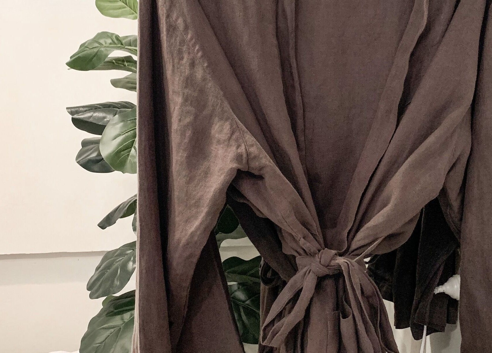 Brown robe hanging at Oura Day Spa, Gisborne, NZ with lush plant backdrop emphasizing relaxation.