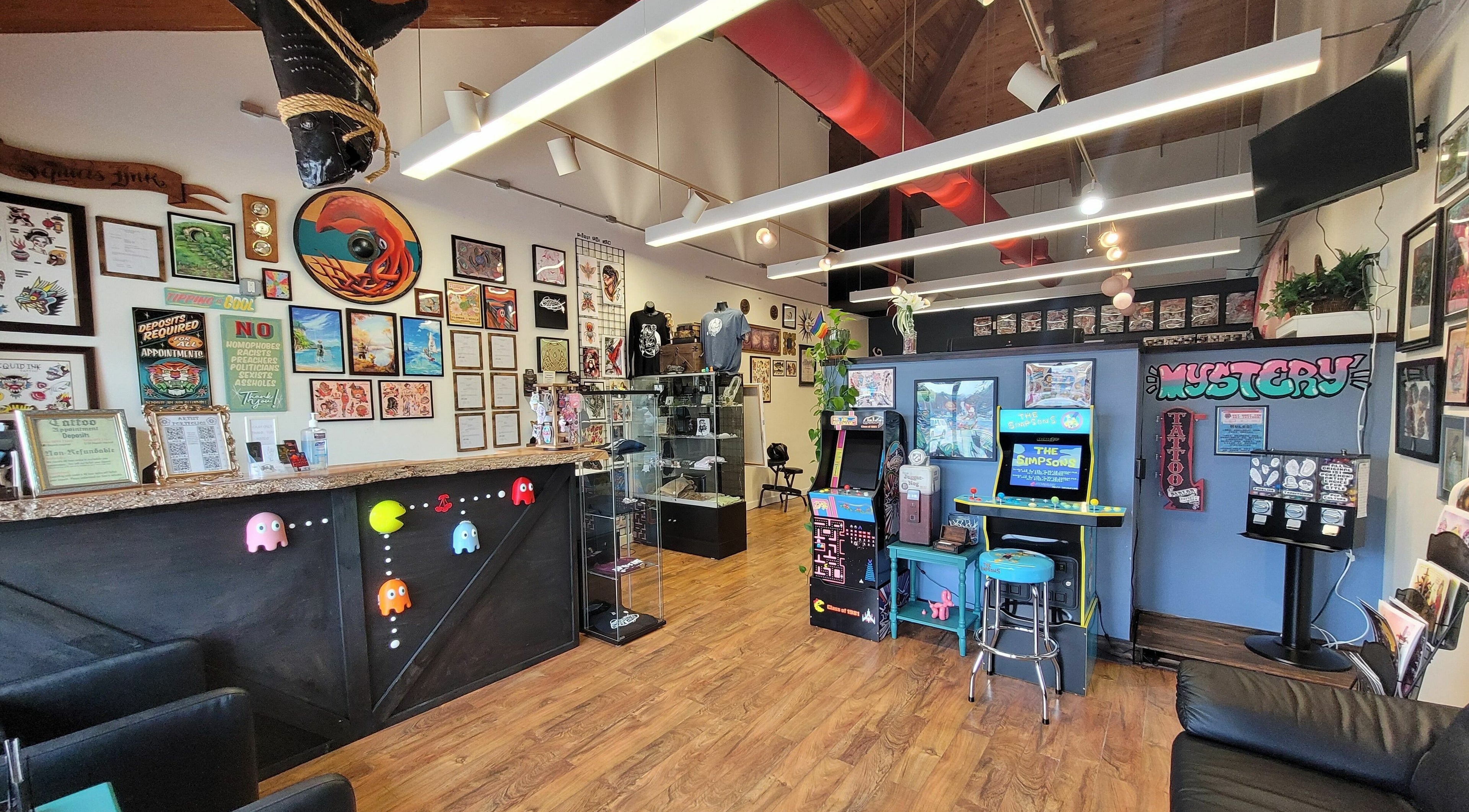 Inviting interior of Squid's Ink Tattoo in Pembroke, Massachusetts featuring arcade games and artistic decor.