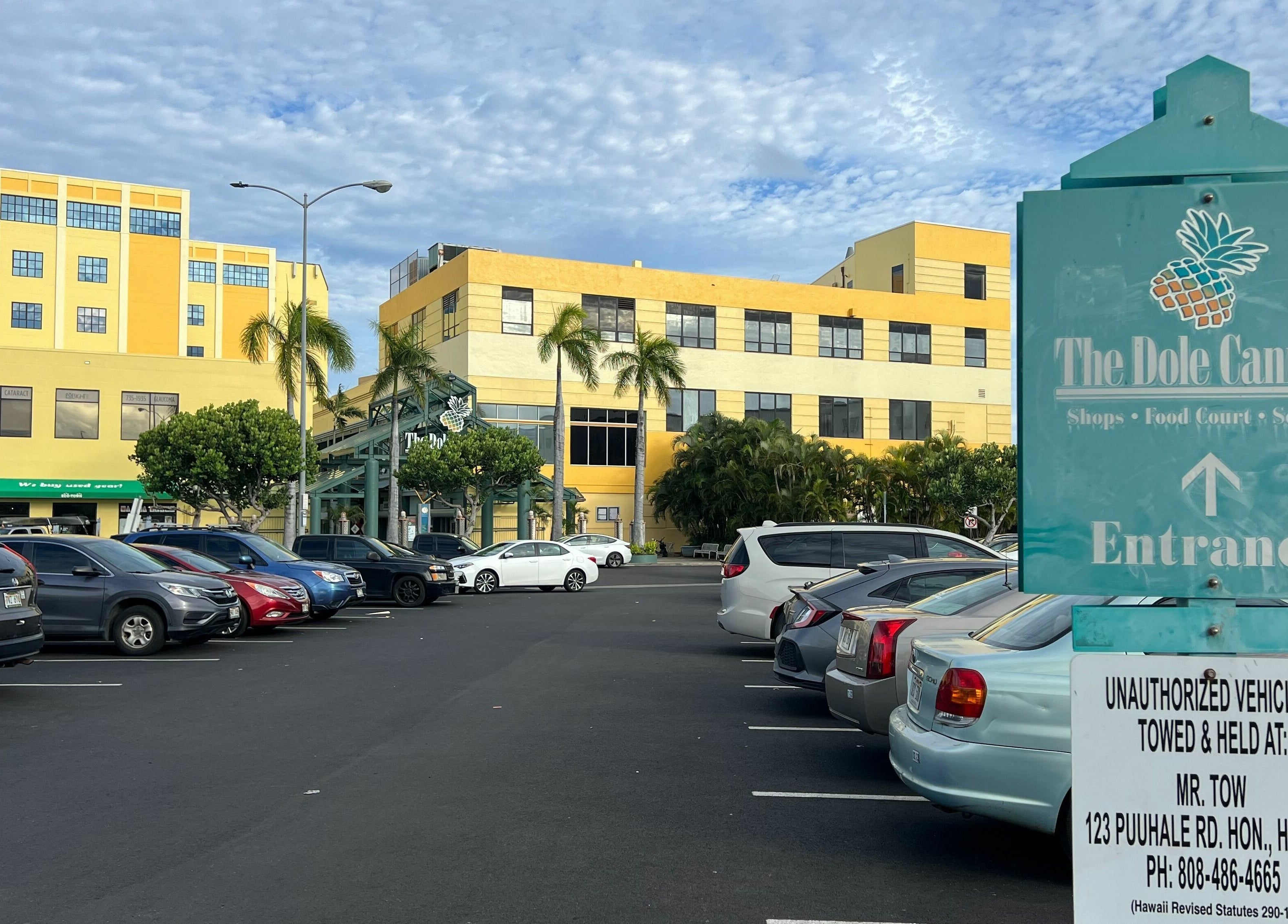 View of the Dole Cannery entrance near Honolulu Nails & Aesthetics Academy, Honolulu, Hawaii with parked cars.