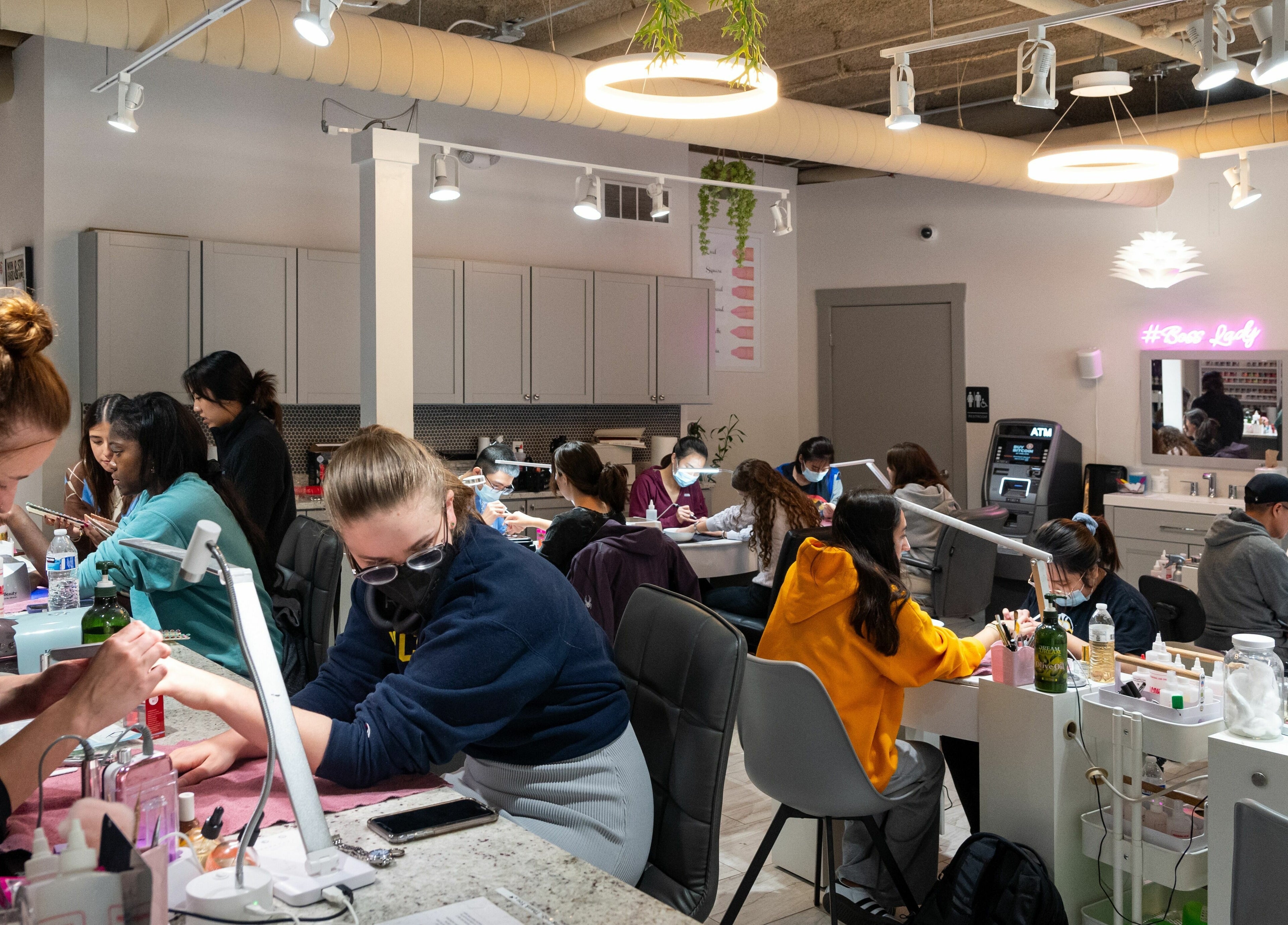 Clients receiving nail services at BeeQ Downtown A2, Ann Arbor, Michigan, US in a lively salon setting.