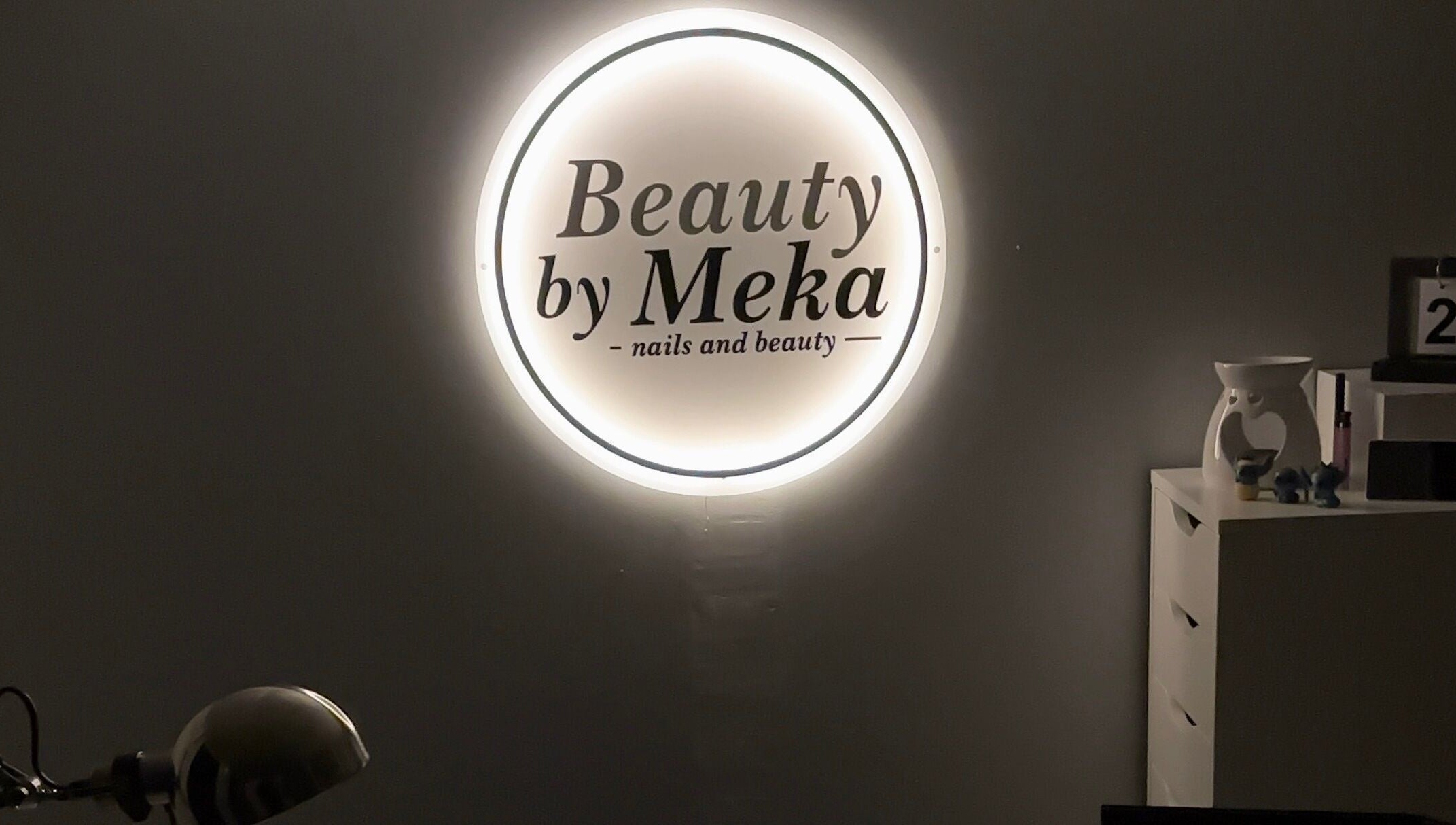 Illuminated logo of Beauty by Meka - Home Salon, Kirkcaldy, Scotland, GB, on a dark wall.