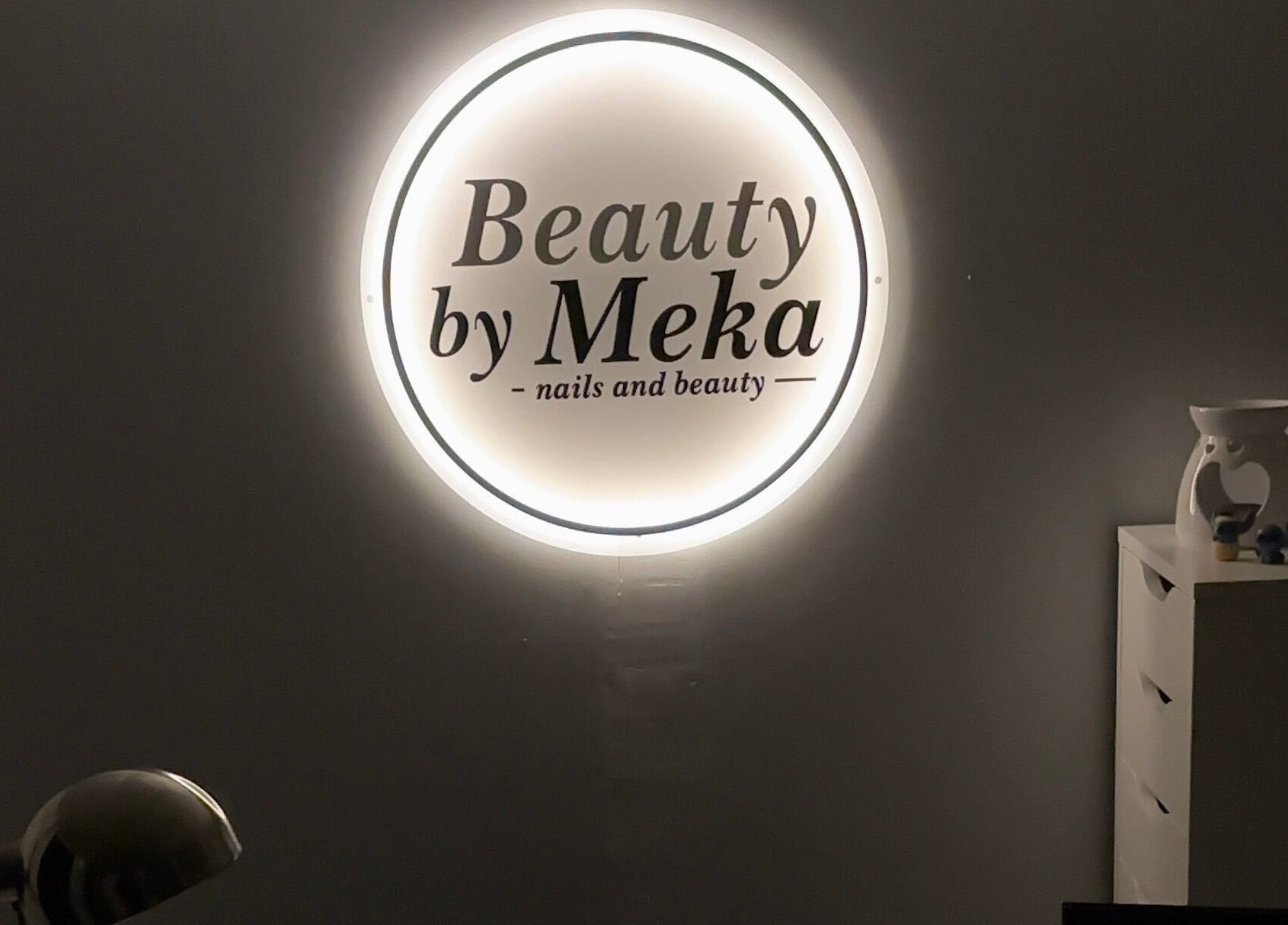 Illuminated logo of Beauty by Meka - Home Salon, Kirkcaldy, Scotland, GB, on a dark wall.