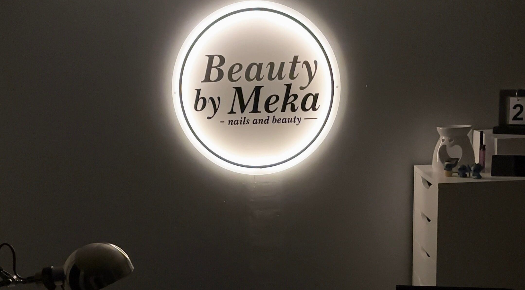 Illuminated logo of Beauty by Meka - Home Salon, Kirkcaldy, Scotland, GB, on a dark wall.