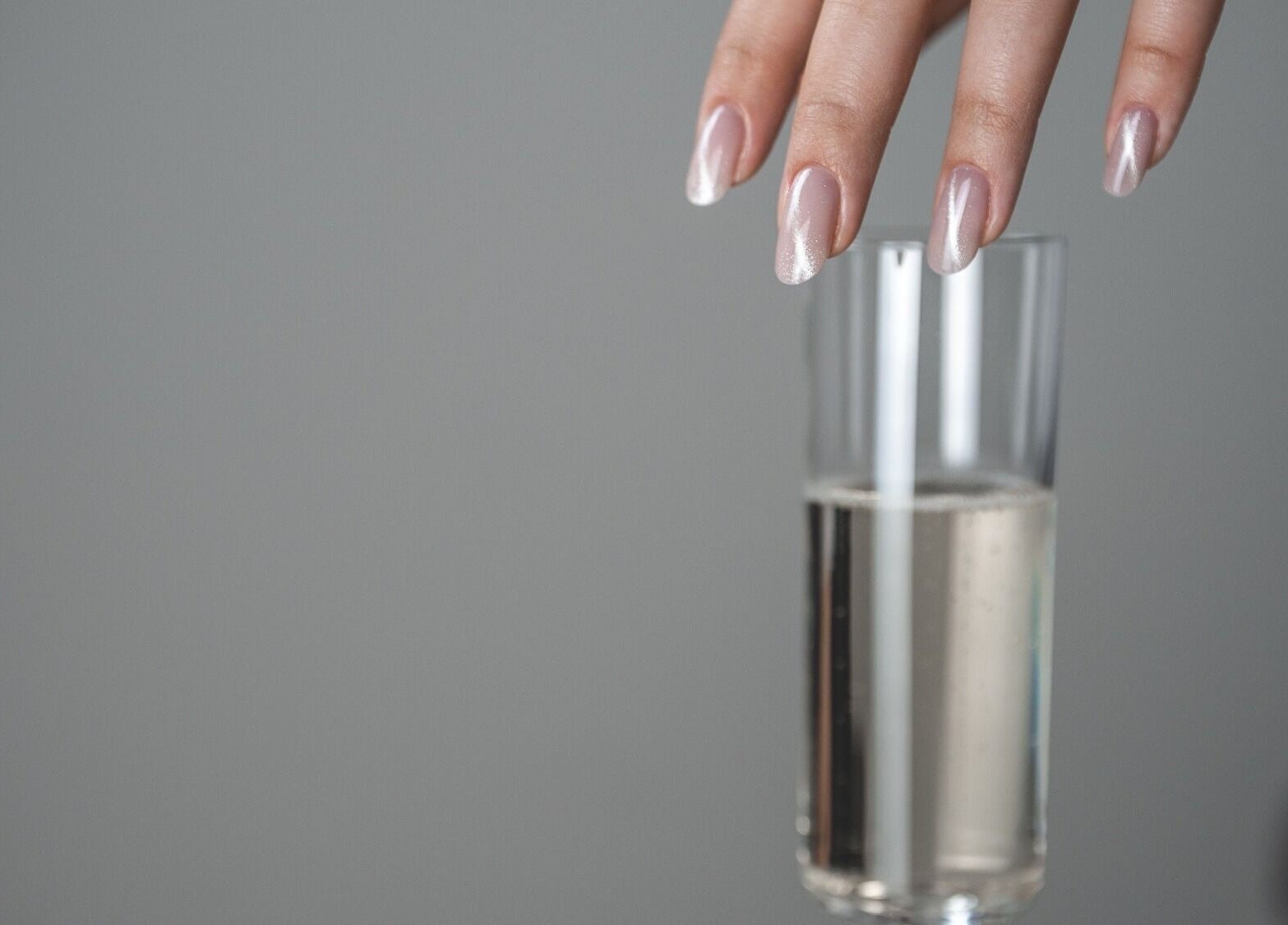 Elegant, manicured hand above a glass at Nails Murr Luxe - Manicure Salon in Canary Wharf, London, England, GB.
